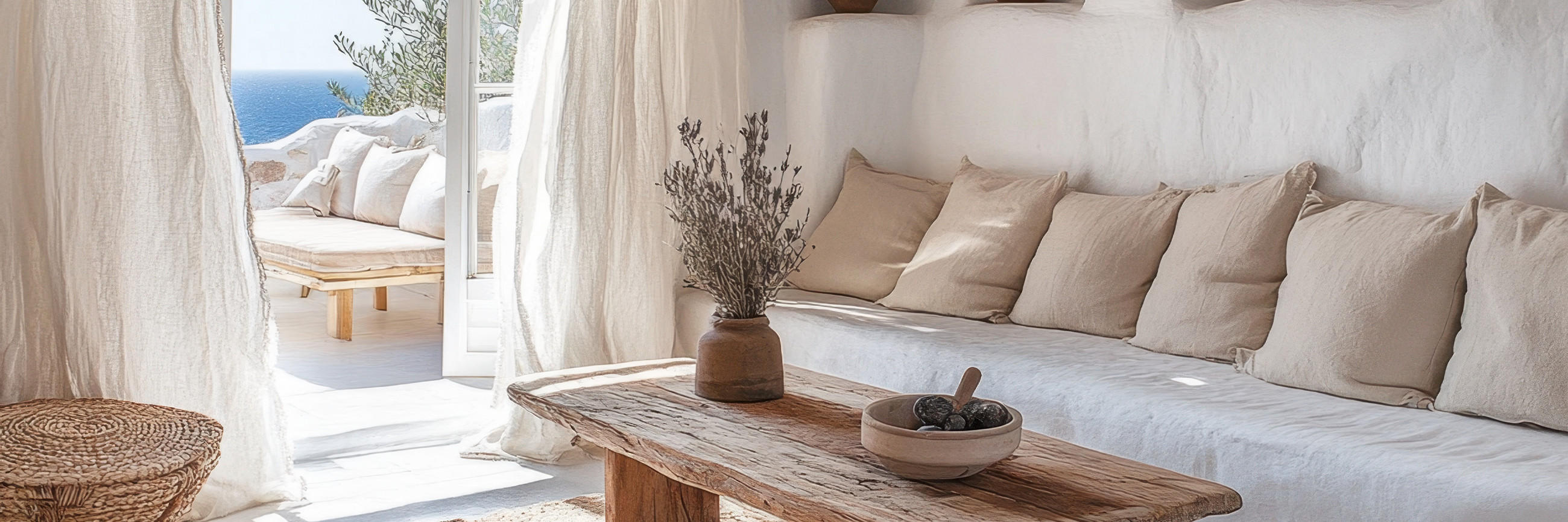 Helles Wohnzimmer mit weißem Sofa, beigen Kissen, Holztisch und Zugang zu Terrasse mit Meerblick