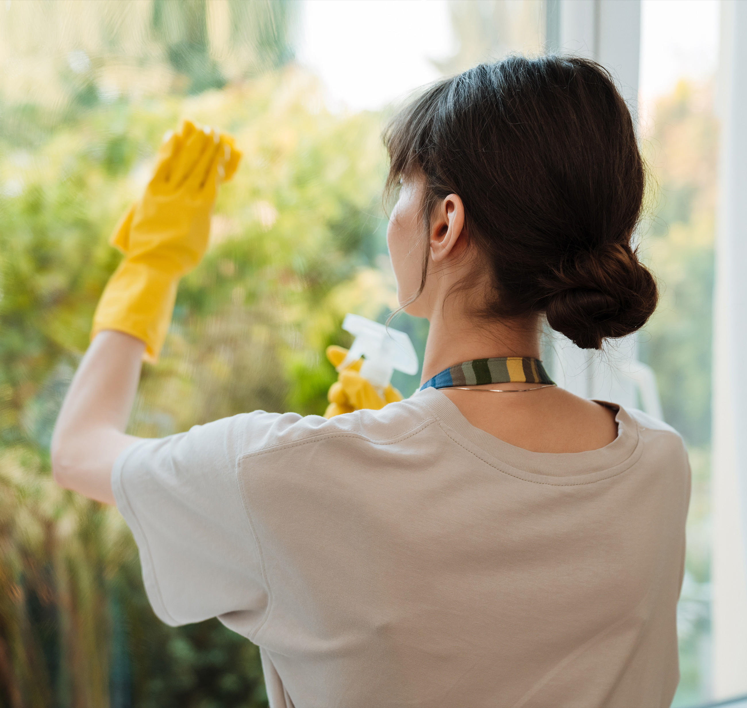  Eine Frau in gelben Handschuhen und weißem Shirt reinigt ein Fenster