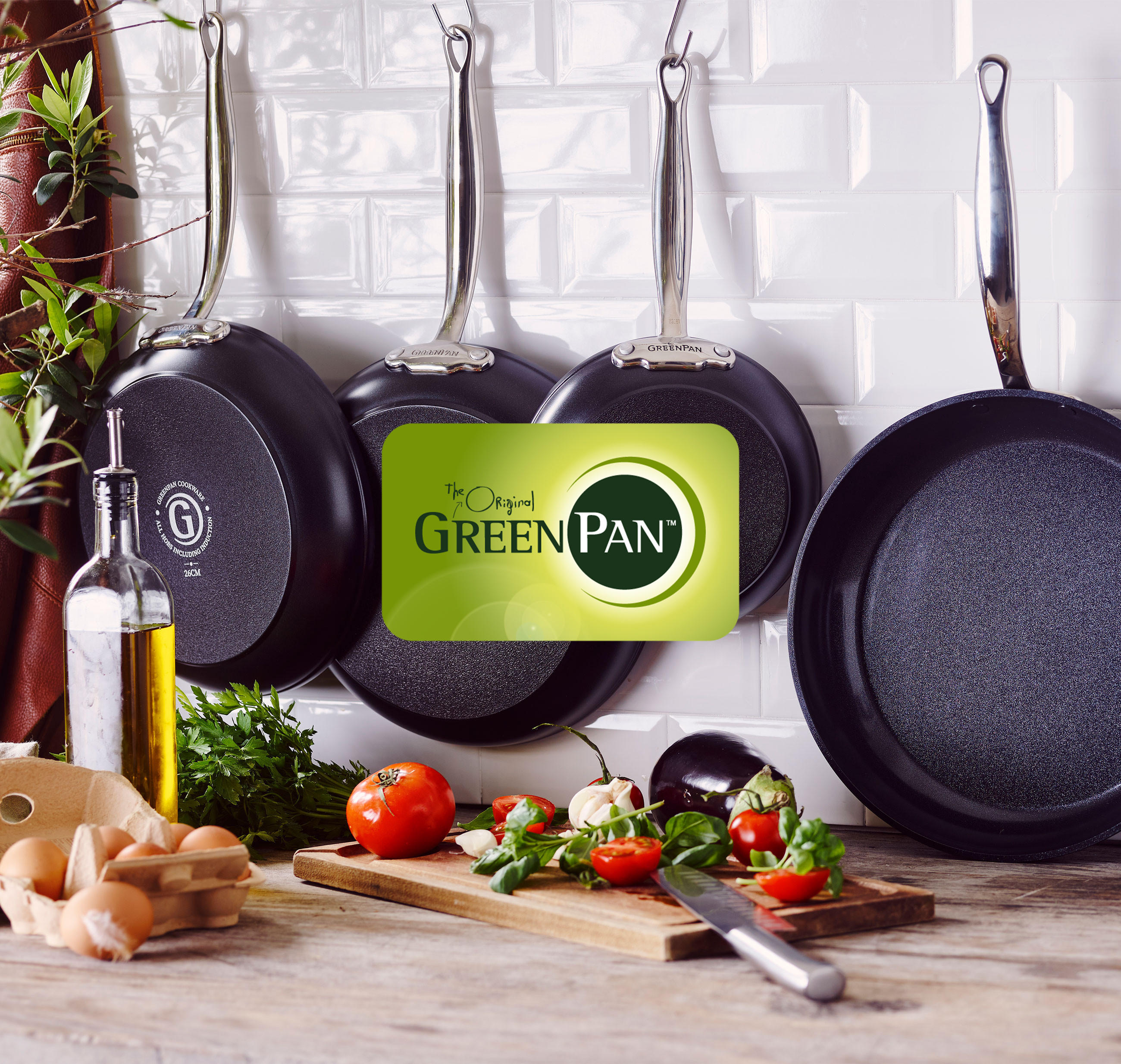 Eine Gruppe von Pfannen der Marke "GreenPan", die an einer Wand hängen.