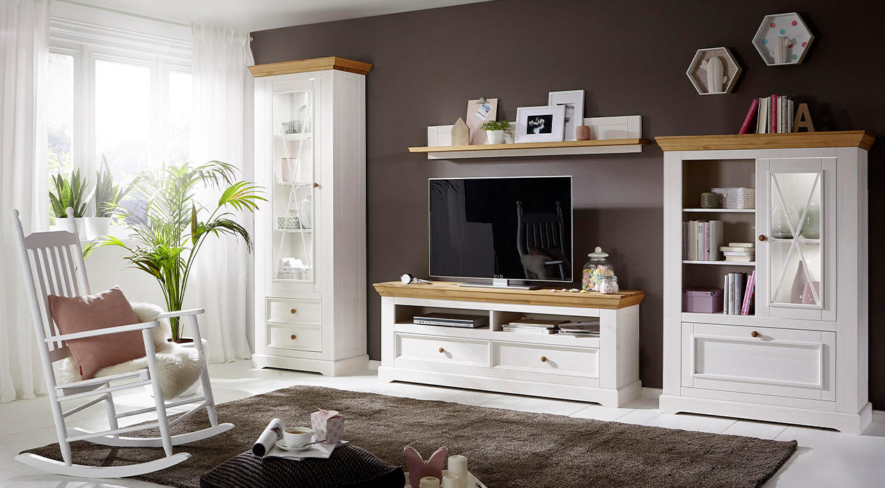 Weiße Wohnwand mit hellen Holzelemente im Landhausstil mit Schaukelstuhl davor.