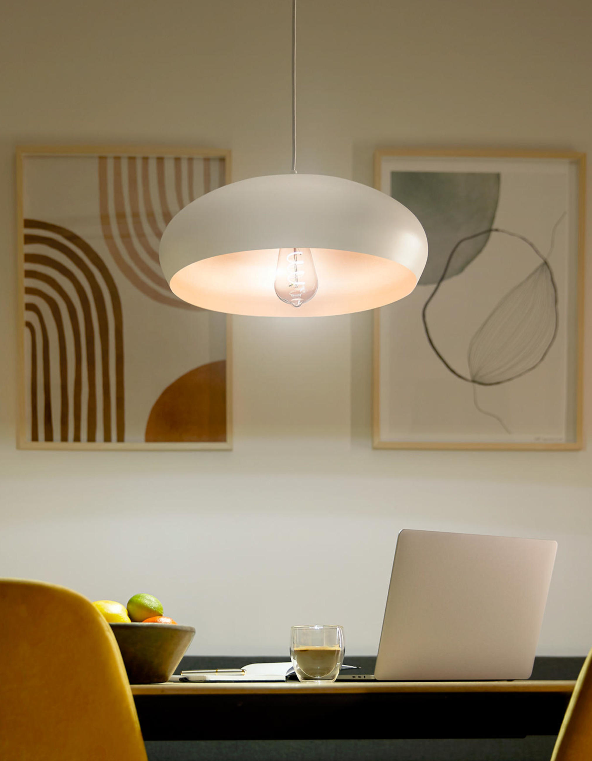Moderne PHILIPS Pendelleuchte mit breitem, weißem Schirm und warmem Licht über einem Esstisch; im Vordergrund Laptop, Glas und Obstschale, im Hintergrund zwei gerahmte Grafiken an der Wand.