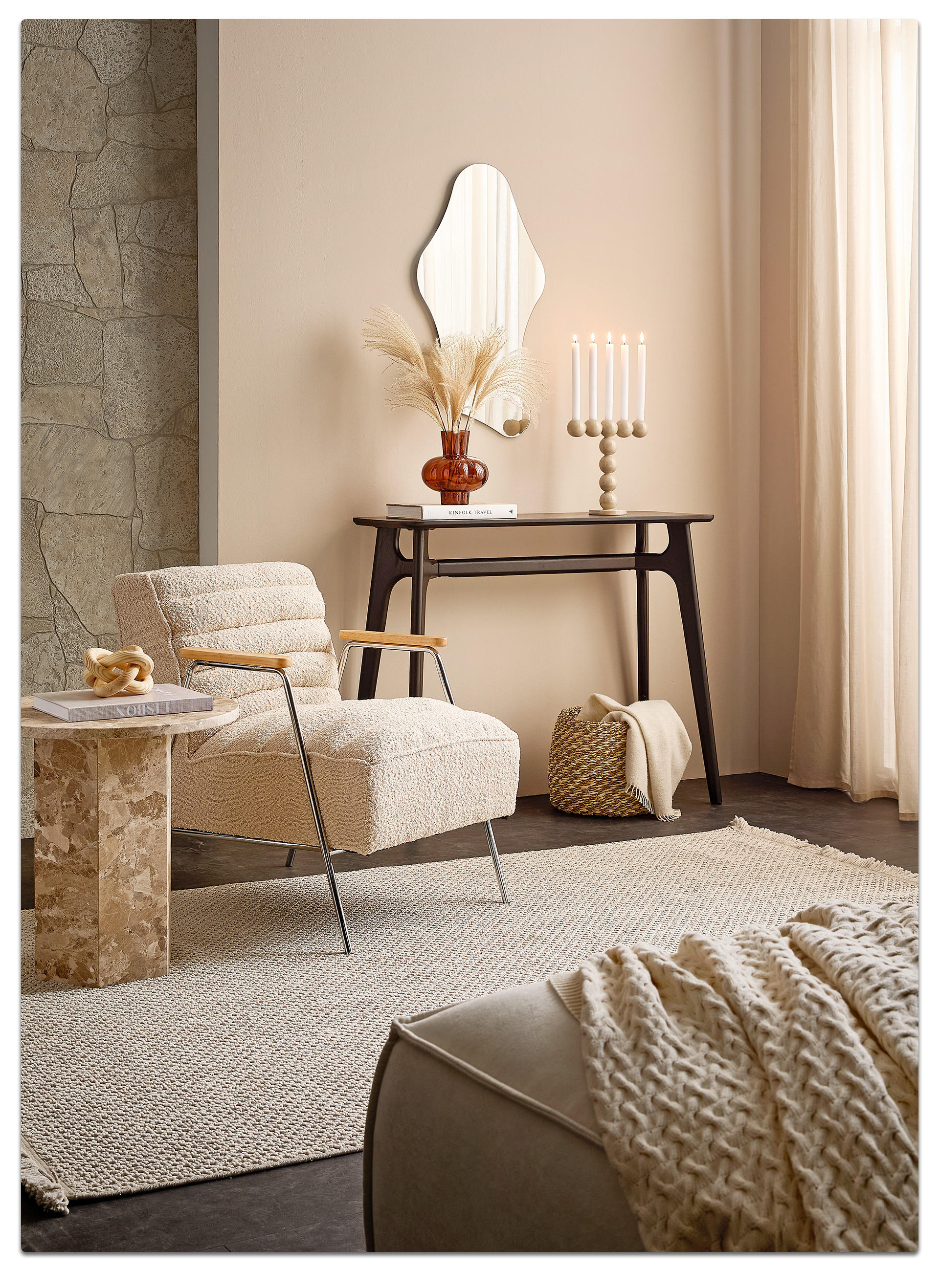 Gemütlich eingerichtete Wohnszene mit beigem Sessel, Marmorseitenta​sch, hellem Teppich, Deko‑Konsole mit Kerzen und Trockenblumen sowie weichen Textilien in warmen Naturtönen.