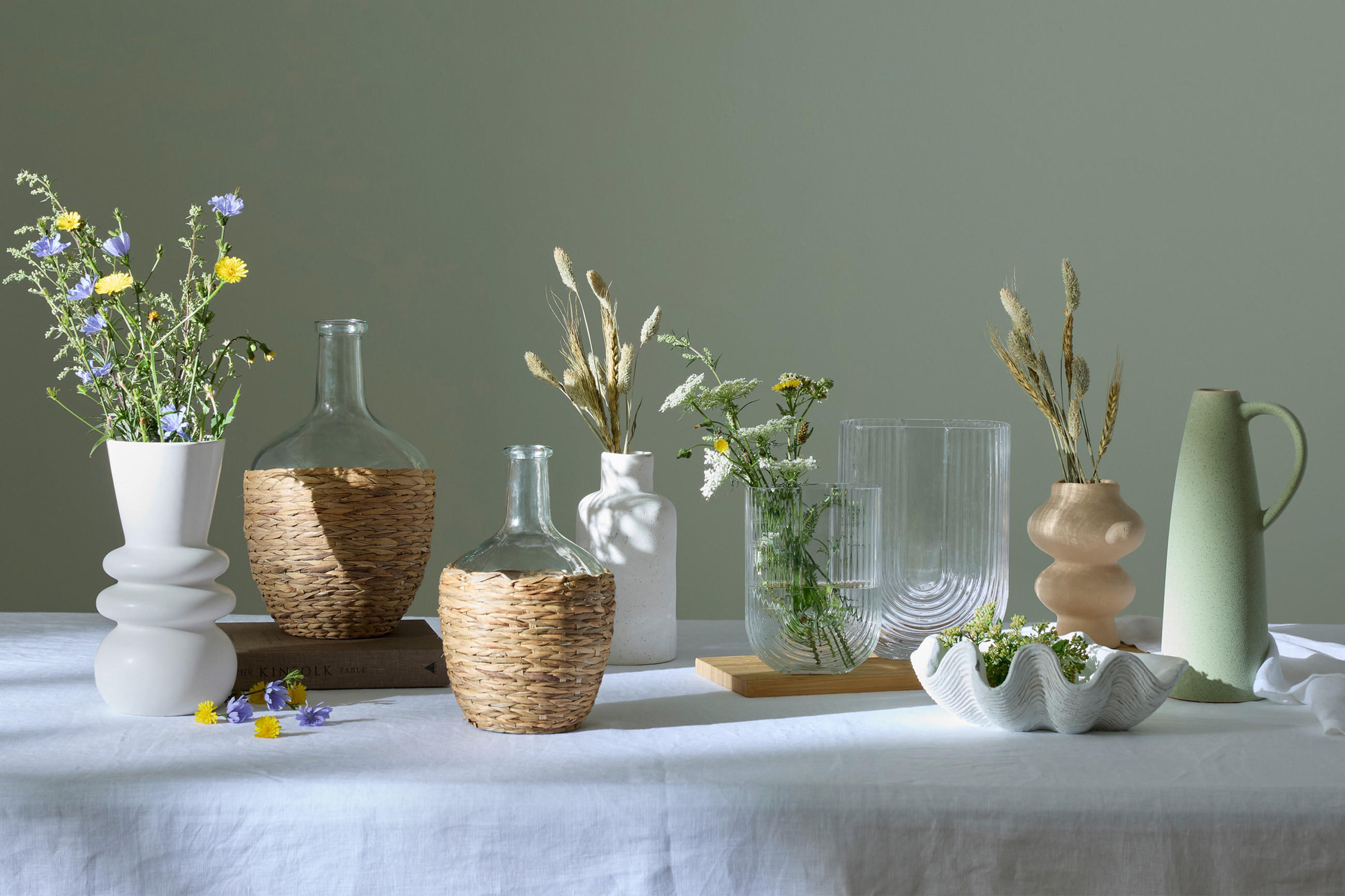 Frühlinghafte Blumendekoration mit Vasen hinter einer Salbei grünen Wand