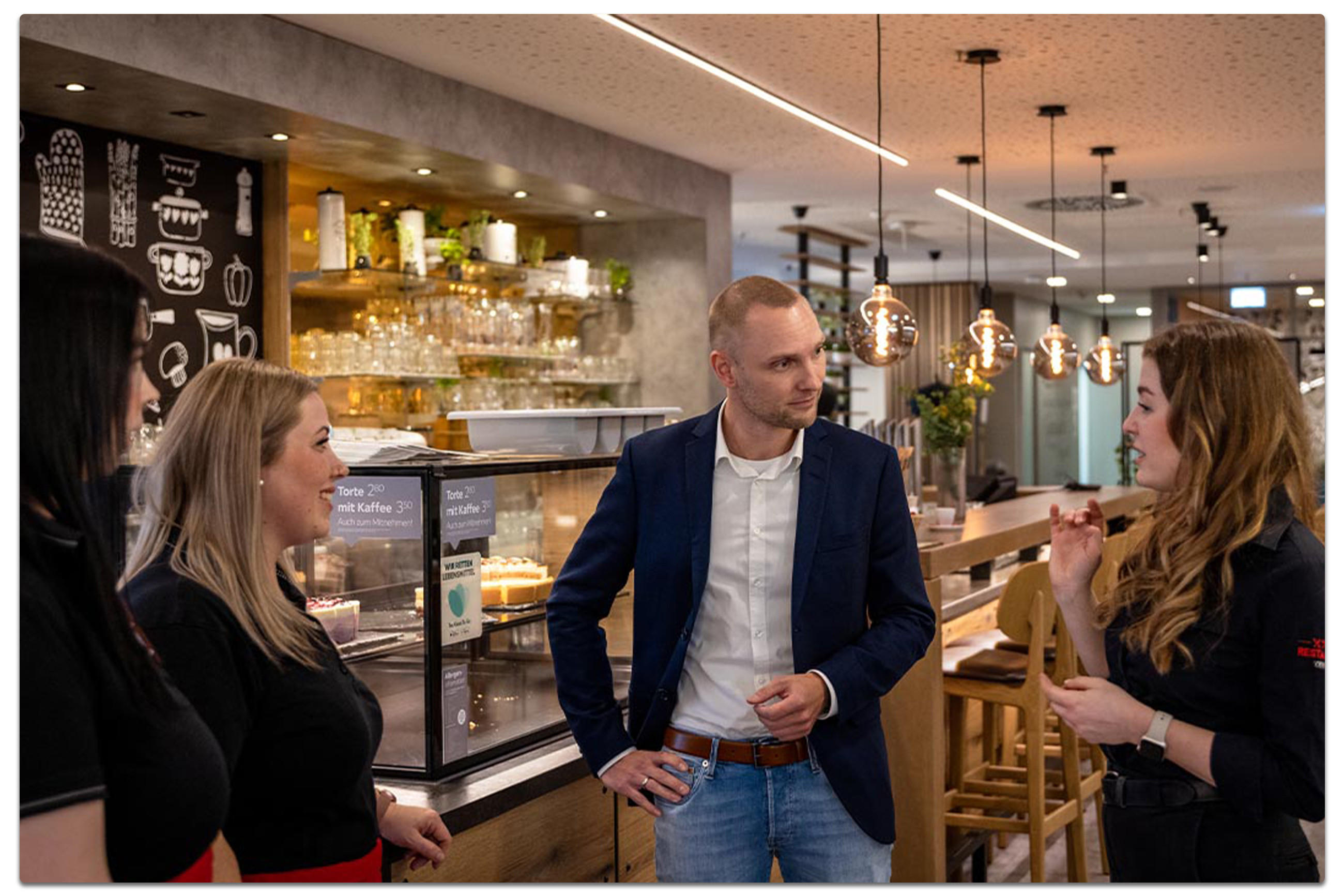 Daniel Balzer und seine Team diskutieren im XXXLutz Restaurant, umgeben von Tischen und einer gemütlichen Atmosphäre.