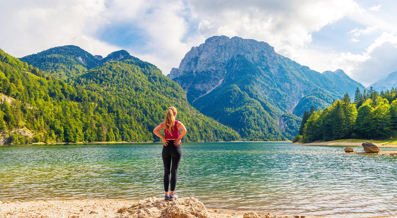 Eine Frau, die Allein vor dem See steht Und die Berge Mit Grüner Natur Betrachtet