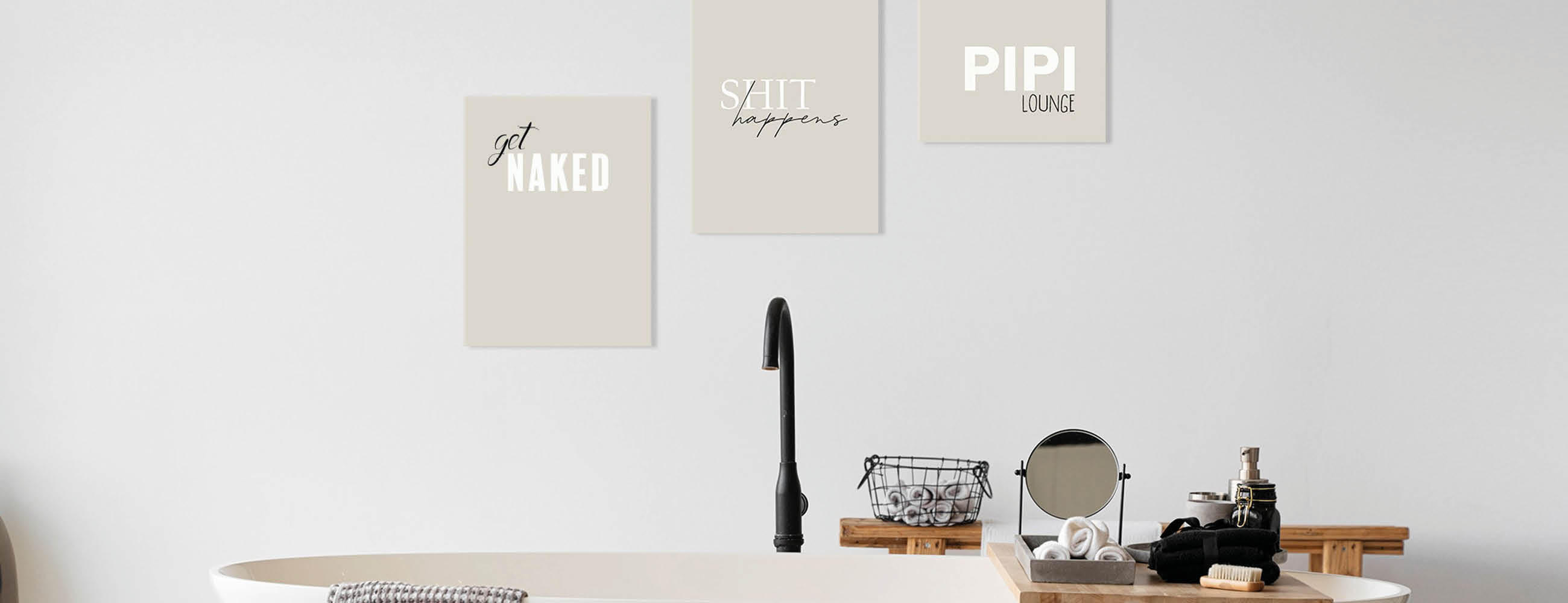 Freistehende Badewanne mit schwarzem Wasserhahn, darüber drei Wandbilder mit den Texten 'get NAKED', 'SHIT happens' und 'PIPI LOUNGE' in schlichtem Badezimmer mit weißen Wänden