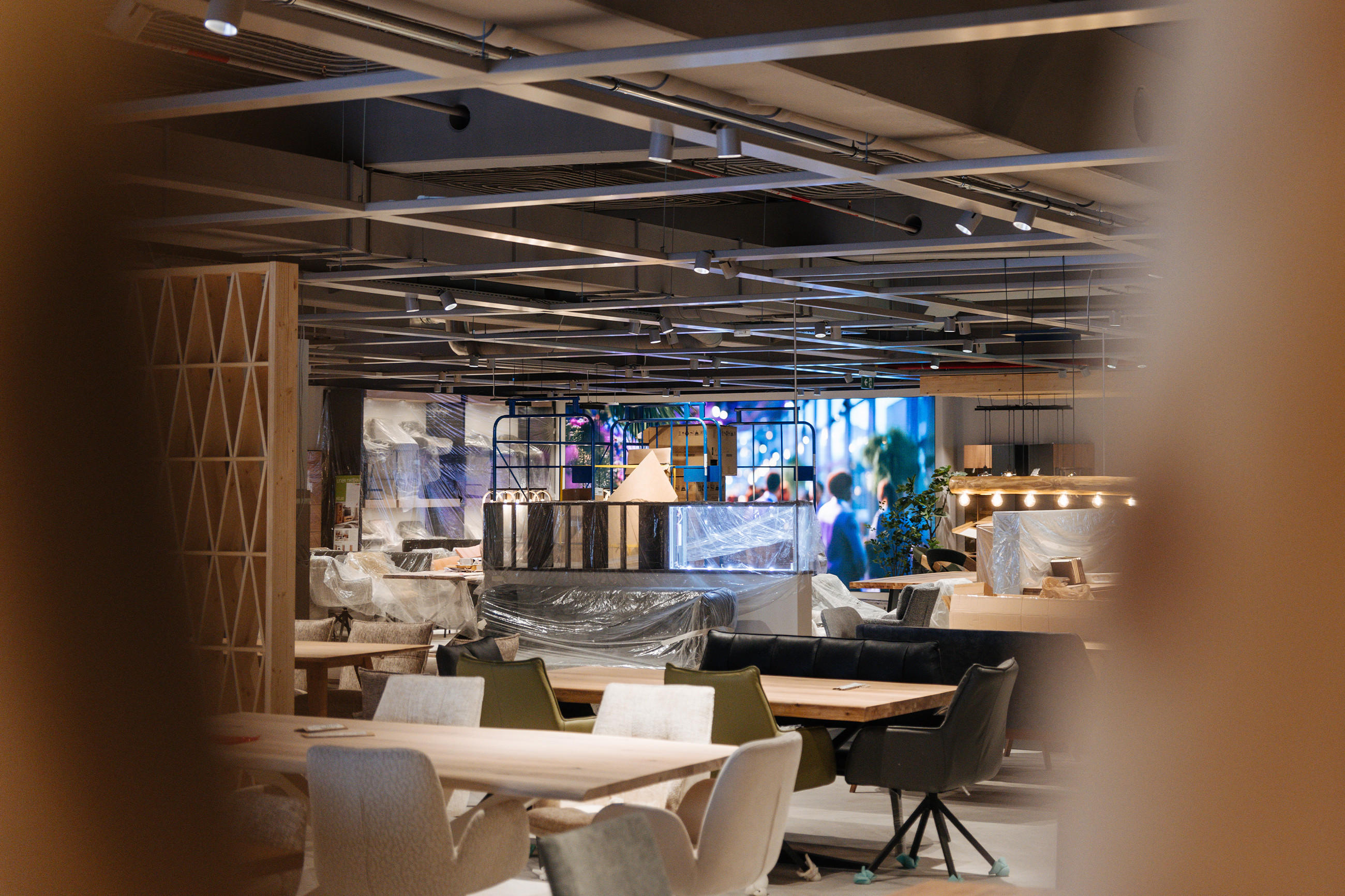 Blick in eine modern eingerichtete Ausstellungsfläche mit verpackten Möbeln, dekorativer Beleuchtung und Raumteilern während einer Eröffnung