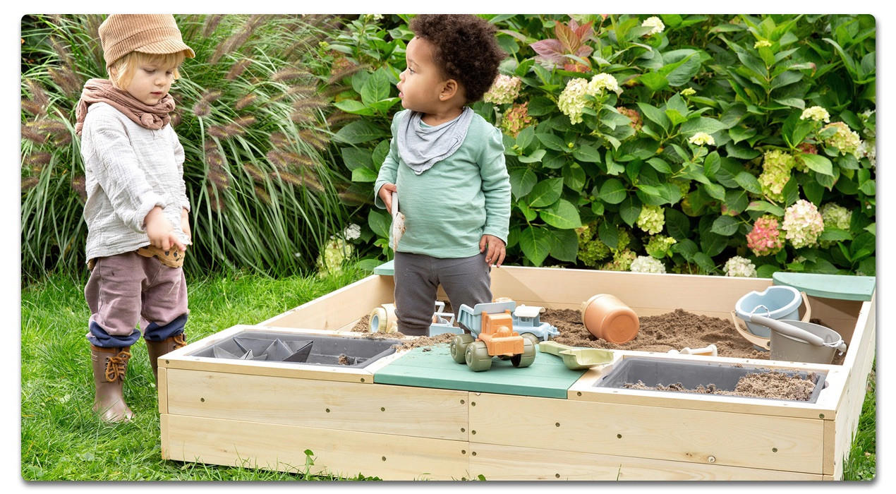 sandkasten mit 2 Kindern und Spielsachen darin