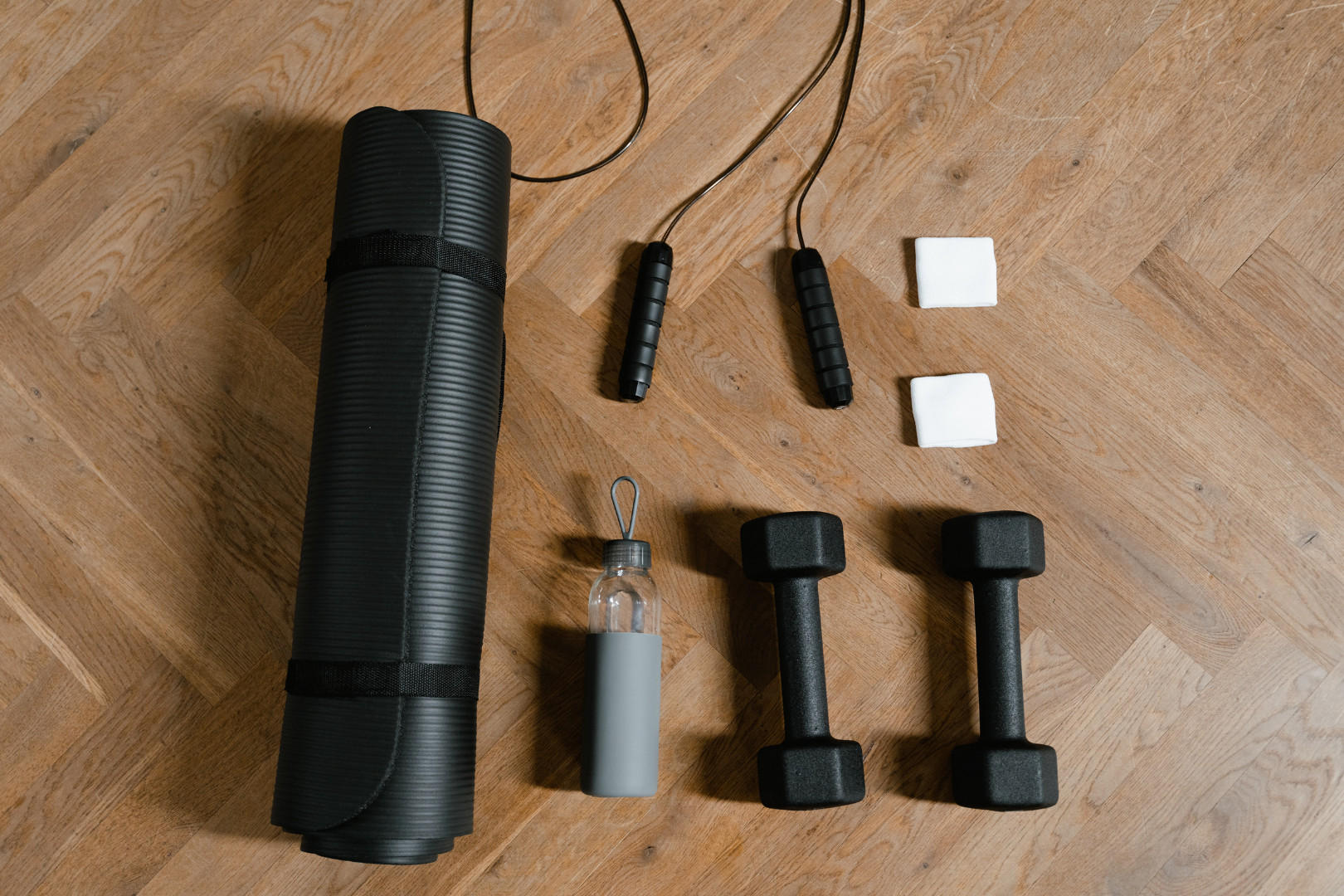 Eine Yoga-Matte, zwei Hanteln und eine Wasserflasche, die für ein Fitness-Workout vorbereitet sind.