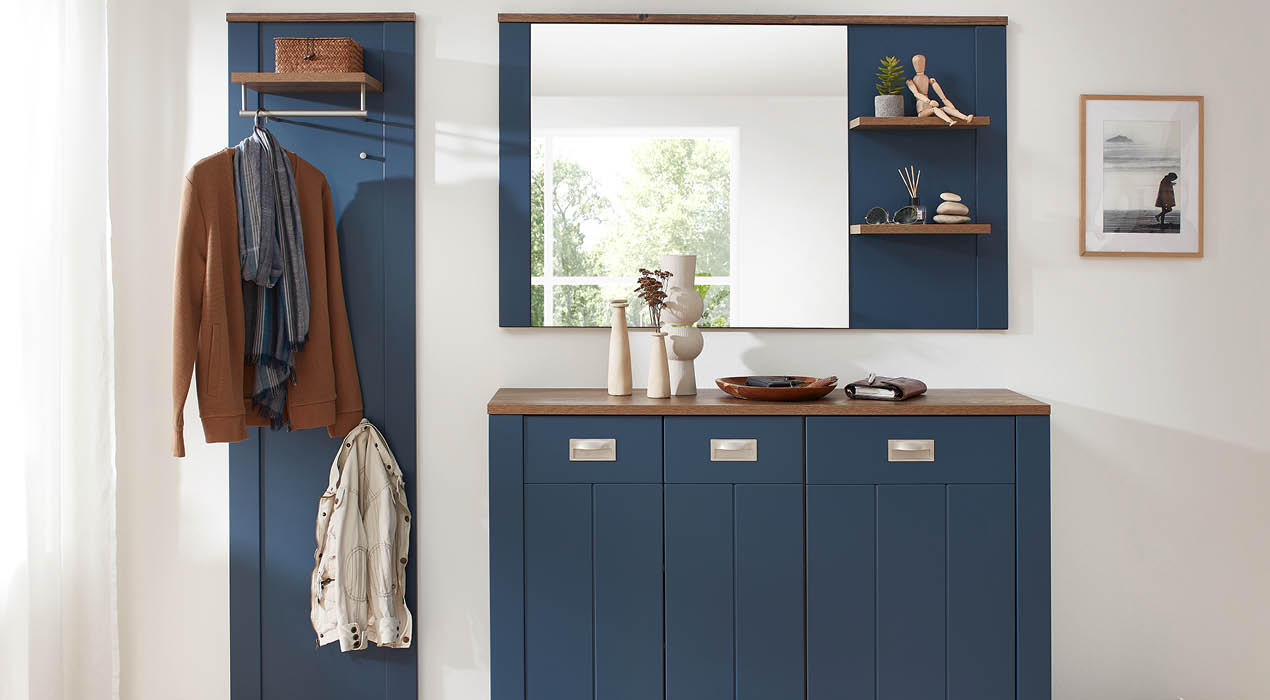 Moderner Eingangsbereich mit blauen Möbeln, darunter eine Kommode mit Spiegel, Garderobe mit brauner Jacke und dekorativen Regalen mit Büchern und Skulpturen
