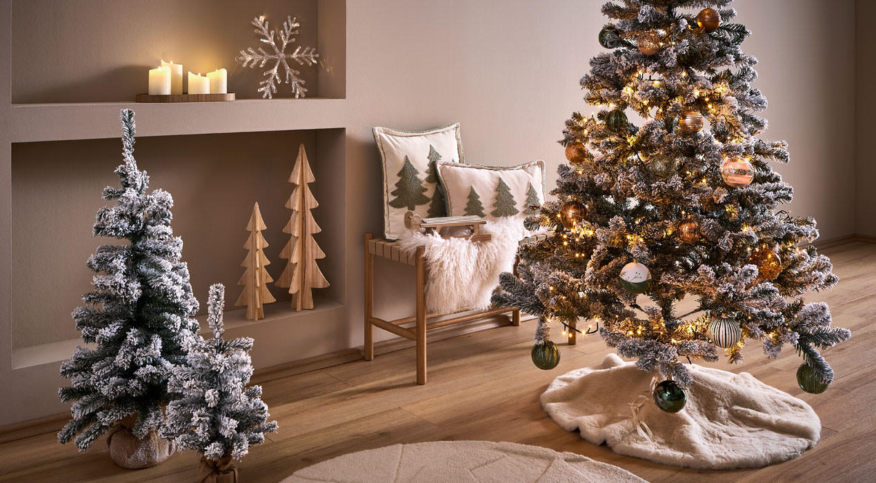 Gemütliches Wohnzimmer mit zwei geschmückten Weihnachtsbäumen, Bank mit Kissen und weihnachtlicher Dekoration.