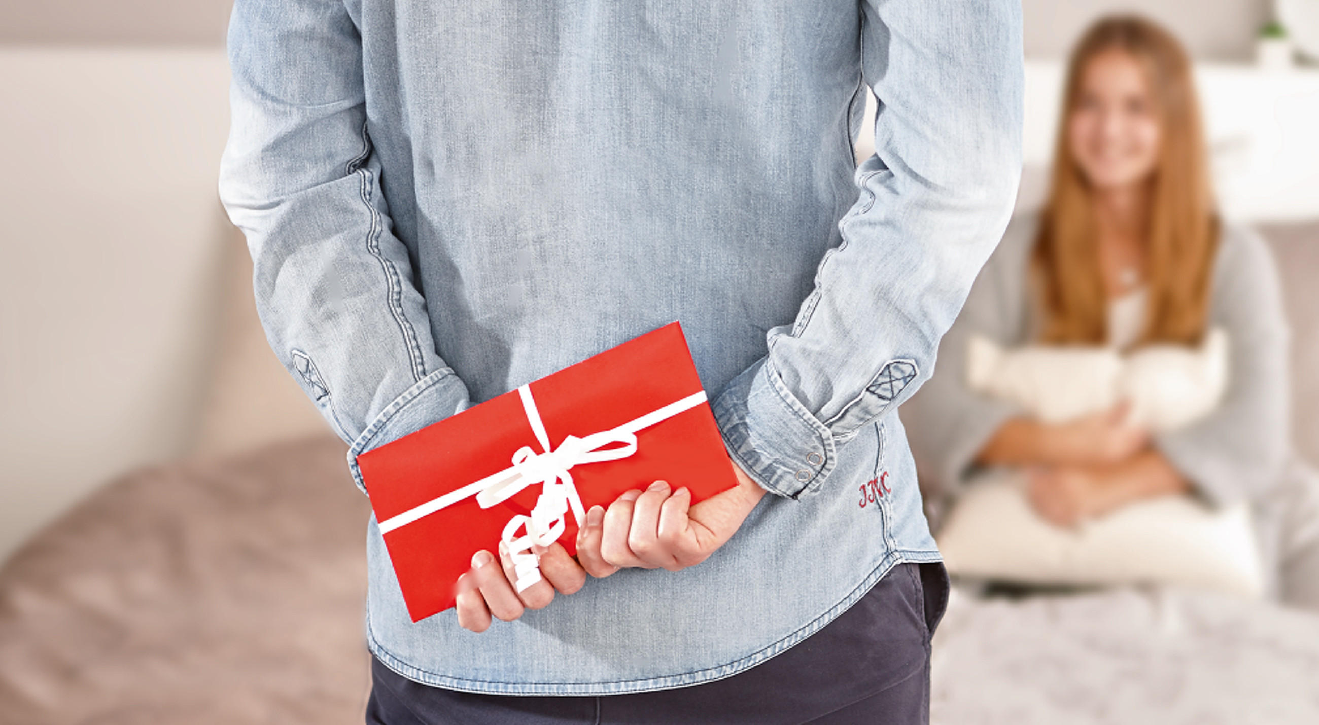  Person mit rotem Geschenkumschlag hinter dem Rücken, daneben vier farbige XXXL-Gutscheinkarten – ideal für stilvolle Geschenkideen rund ums Wohnen.