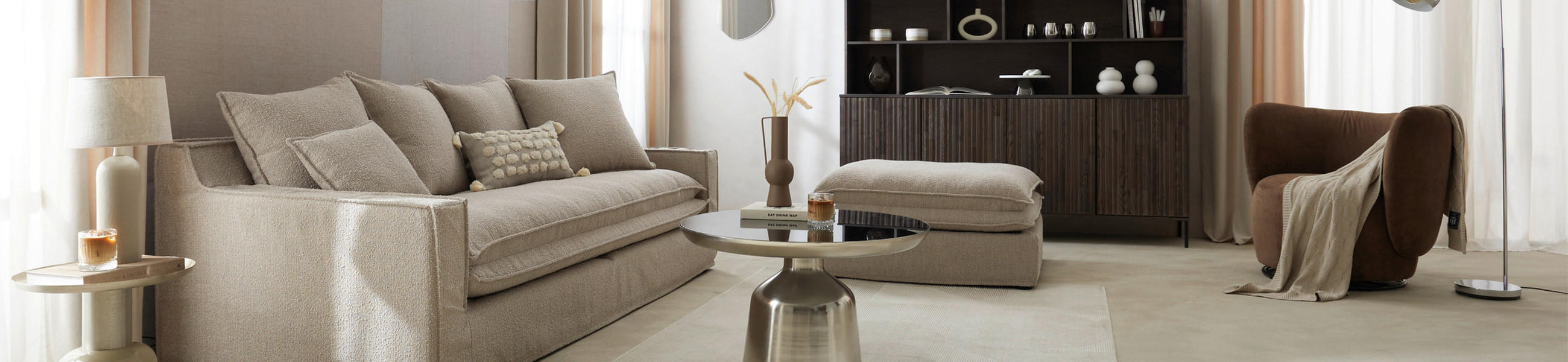 Modernes Wohnzimmer mit beigem Sofa, rundem Couchtisch, braunem Sessel und Regal im Hintergrund