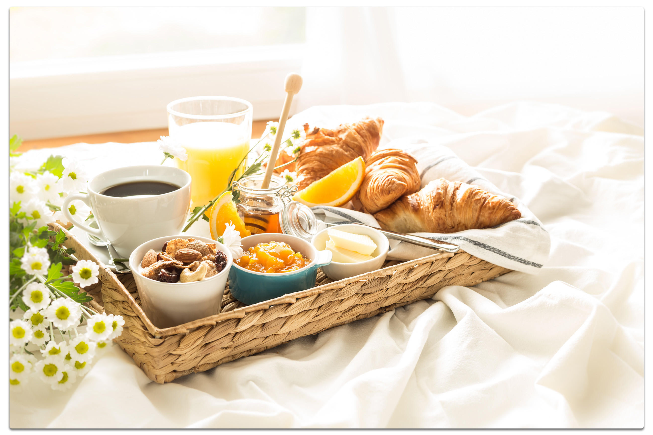 Frühstückstablett auf einem Bett mit Croissants, Orangensaft, Kaffee und weißen Blumen