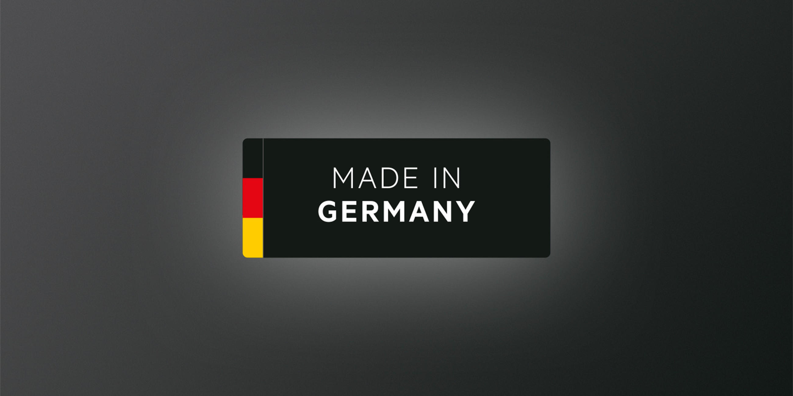 Schwarzes Label mit Deutschlandfarben und der Aufschrift „Made in Germany“ auf dunklem, mattem Hintergrund.