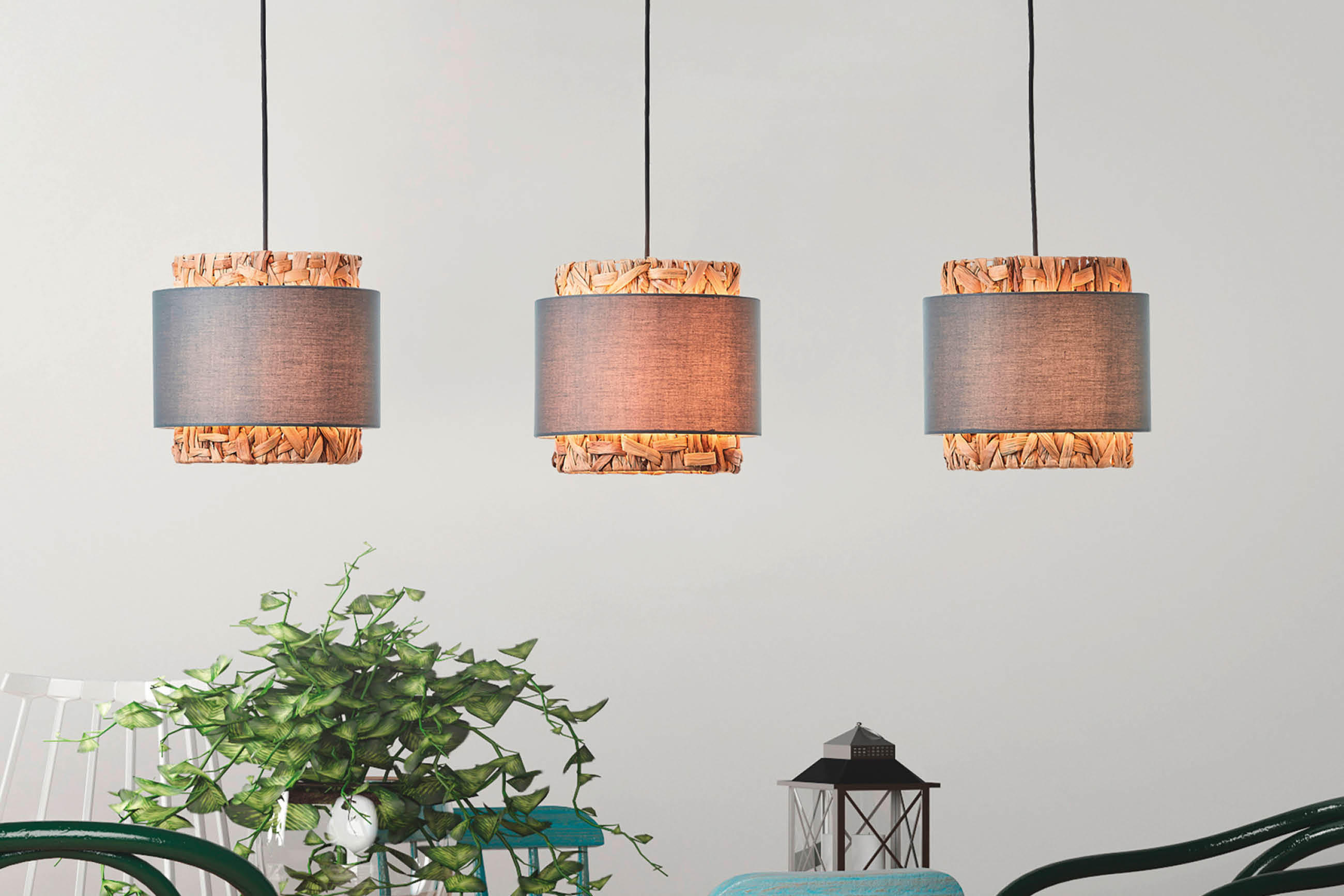 Drei moderne Hängelampen mit grauen Schirmen und dekorativen Holzelementen über einer Einrichtung mit Pflanzen, Stühlen und einer kleinen Laterne.