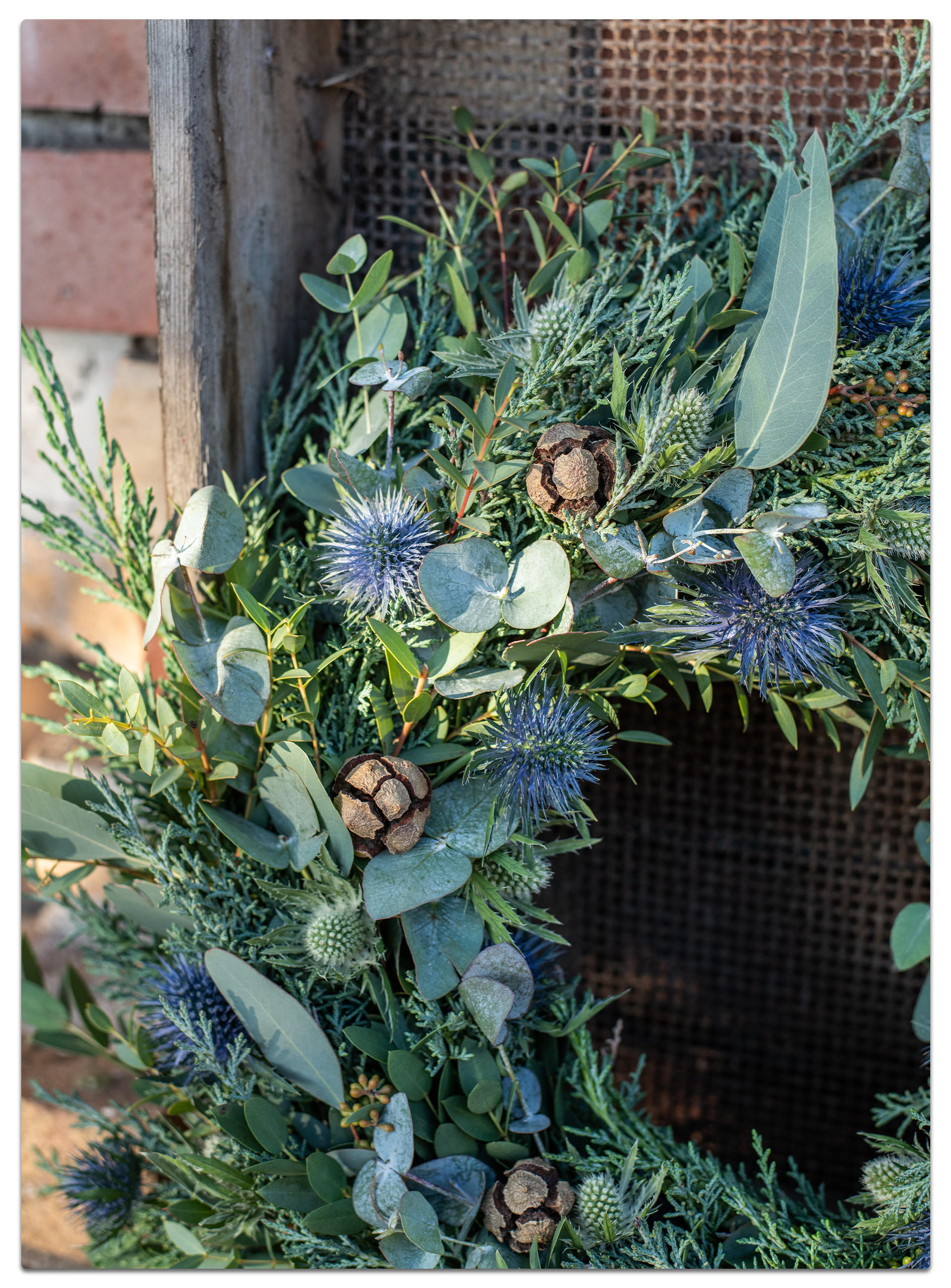 DIY-Kranz mit blauen und grünen Blättern sowie Tannenzapfen, ideal für festliche Dekorationen