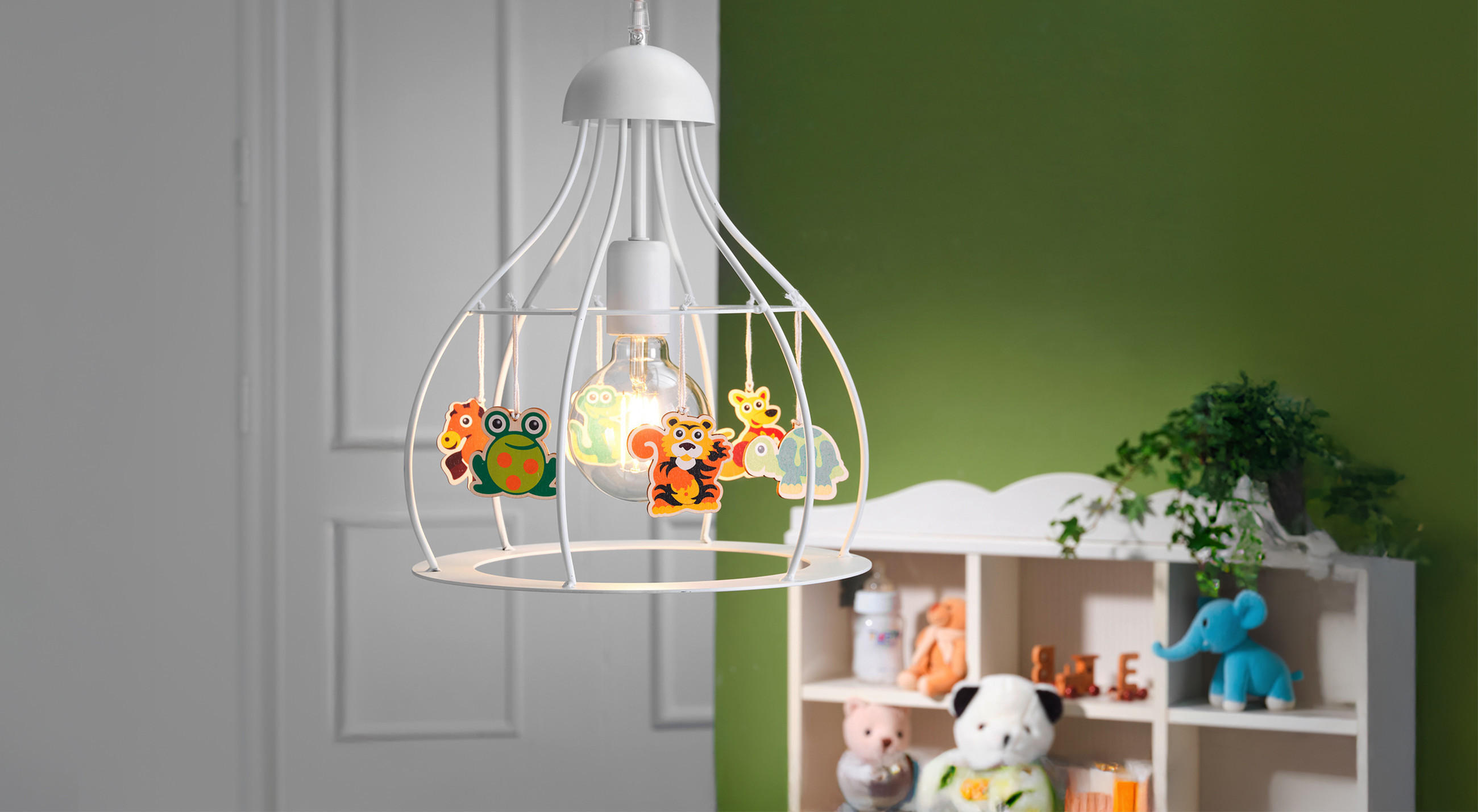 Eine dekorative Kinderzimmer‑Hängeleuchte mit weißem Metallgestell hängt im Raum; an ihr sind bunte Tierfiguren befestigt. Im Hintergrund stehen ein Regal mit Stofftieren, eine weiße Tür vor einer grün‑weißen Wand.