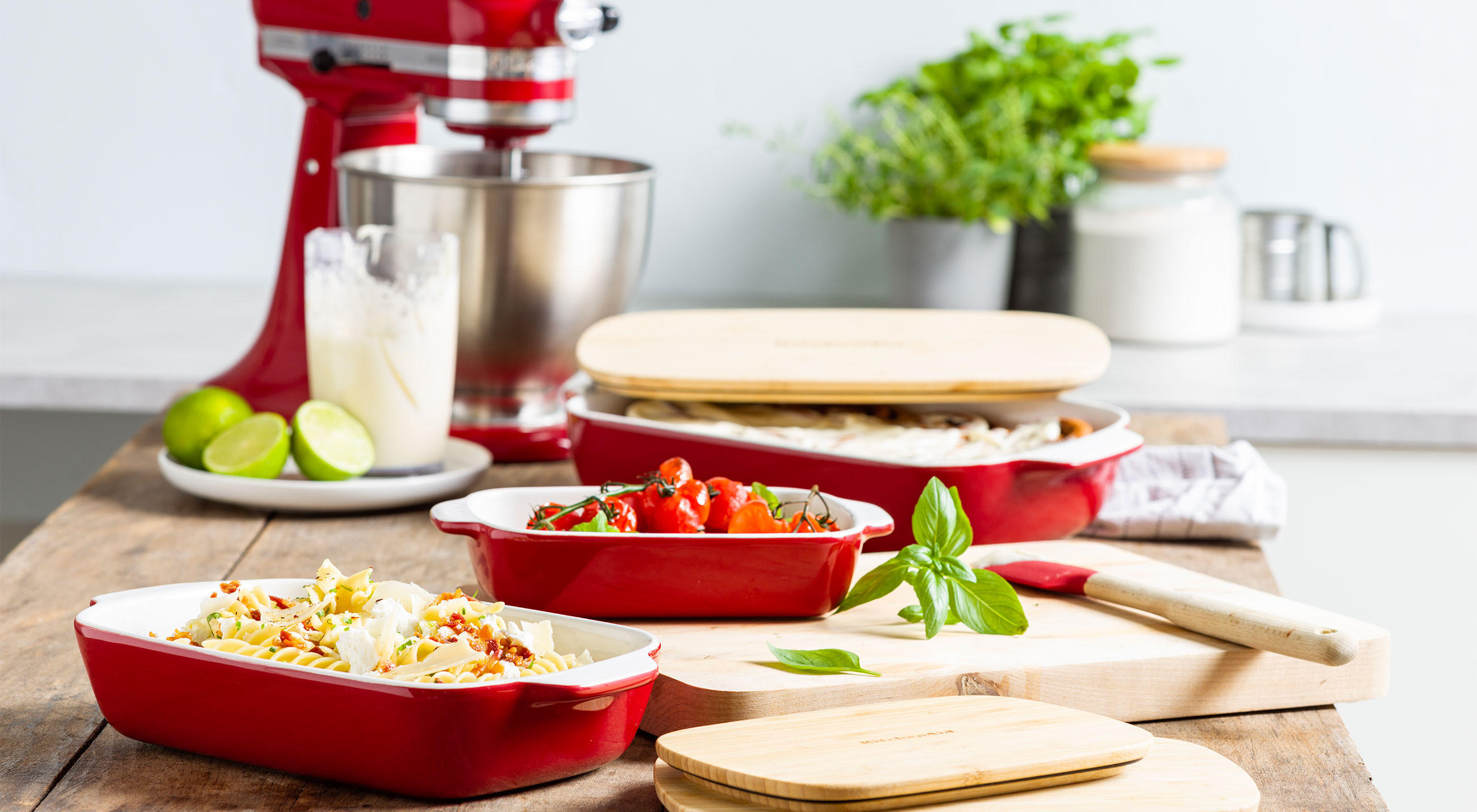 Rotes Geschirr von KitchenAid auf einem Holztablett, das auf einem massiven Holztisch präsentiert wird.