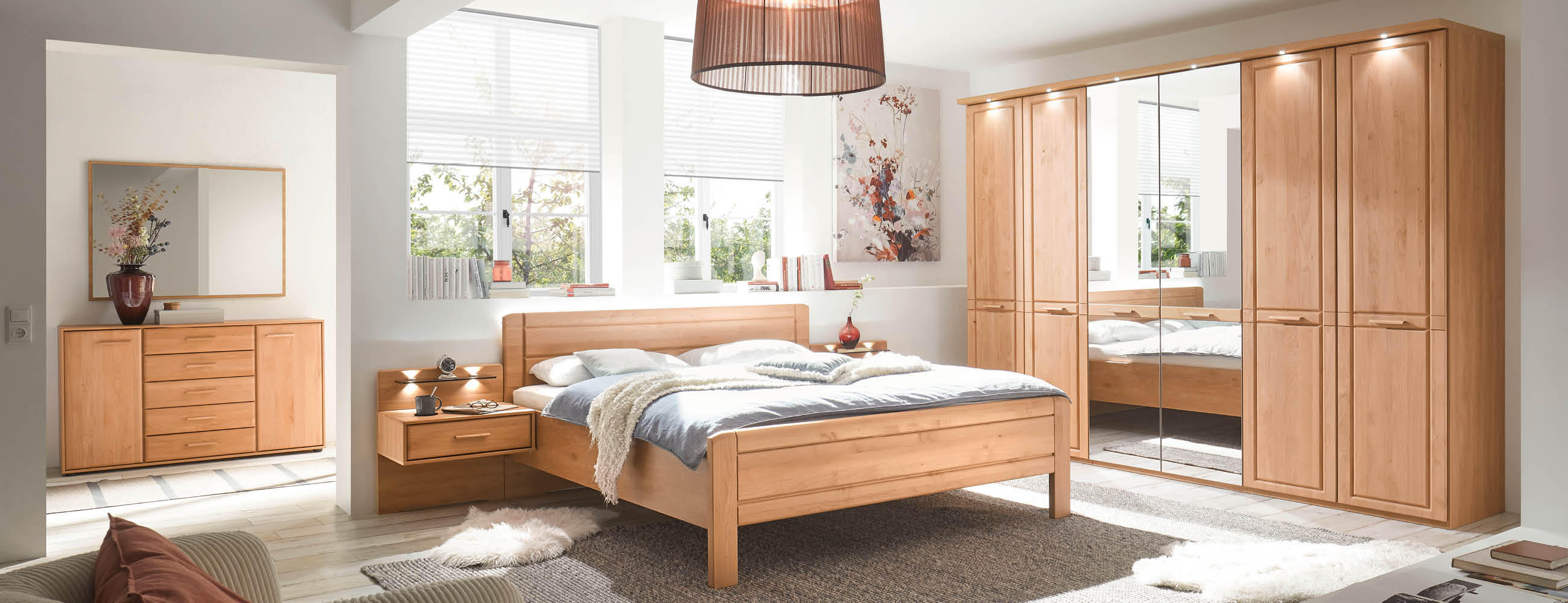 Schlafzimmeransicht mit Bett, Kommode und einem Kleiderschrank aus Holz mit einem Spiegel.