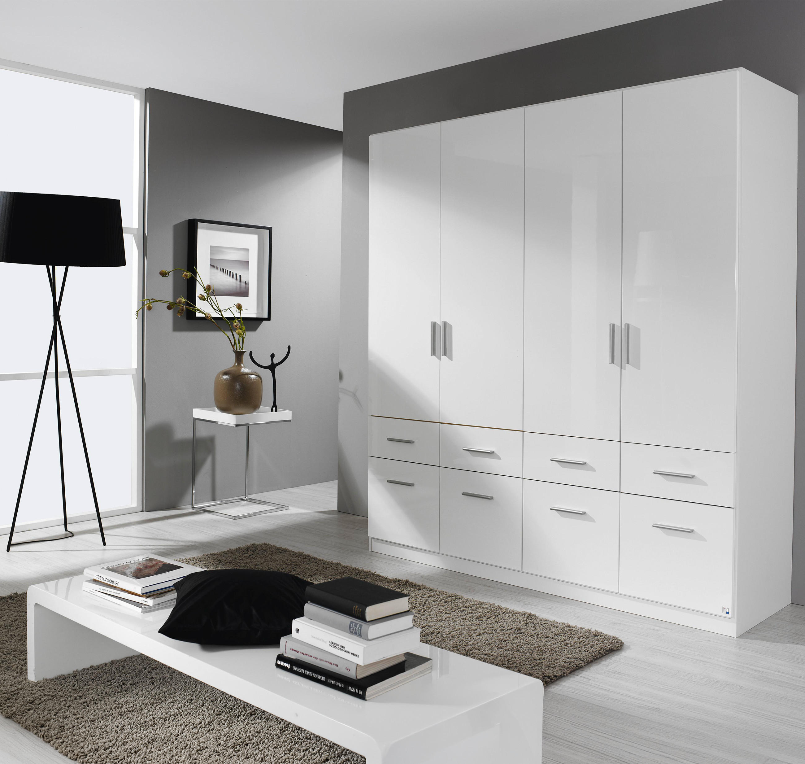 Weißer Kleiderschrank mit Türen und Schubladen in modernem, hellem Raum; daneben schwarze Stehlampe, Beistelltisch mit Vase und Bild.