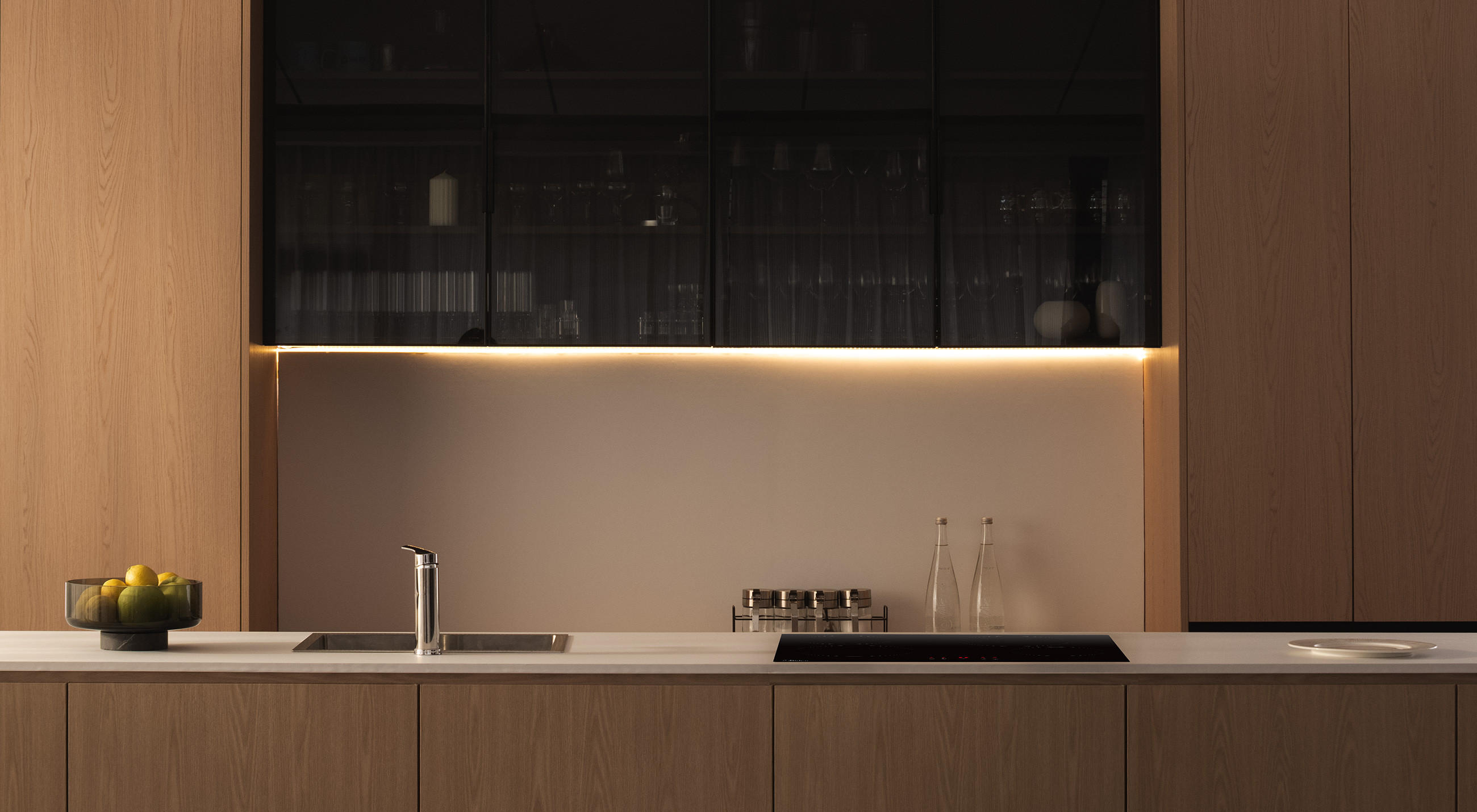 Minimalistische Designküche mit integrierter Spüle und flächenbündigem Midea-Kochfeld auf der Arbeitsplatte; warme Unterbau-Beleuchtung und Holzfronten.