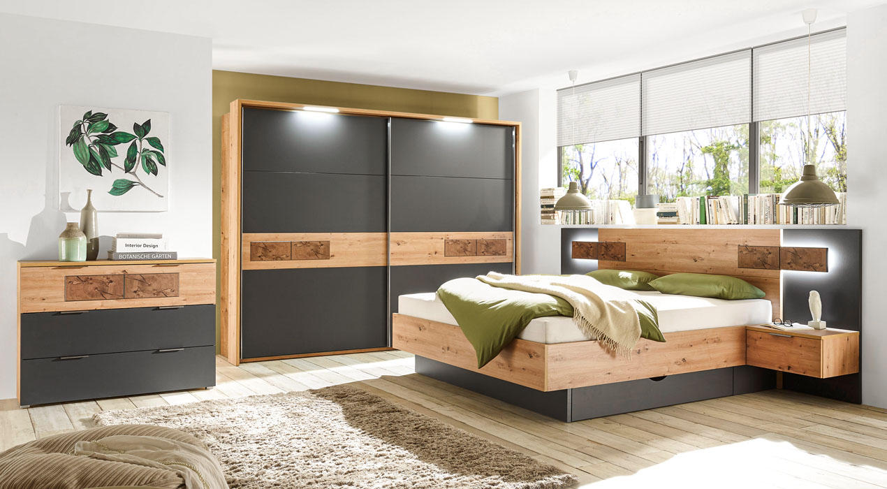 Modernes Schlafzimmer mit Holz- und Schwarztönen, grünem Bettzeug, Schiebetürenschrank mit schwarzen Paneelen und Kommode mit Deko und Pflanzenbild