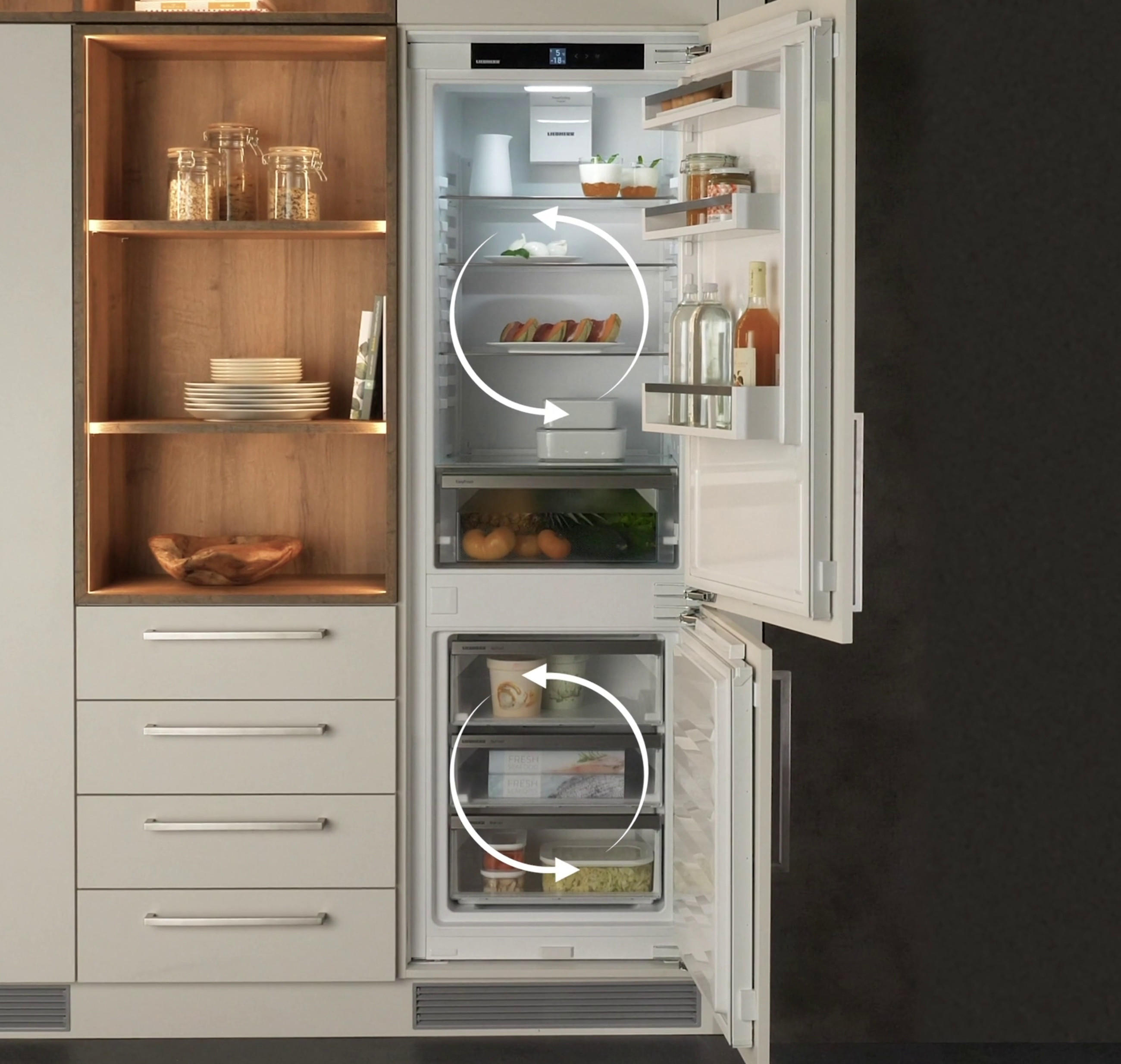 Küche in Naturfarben zeigt offenes LIEBHERR Kühlgerät mit DuoCooling Technologie, welche durch Pfeilen in beiden Kühlräumen symbolisch unterstrichen wird.