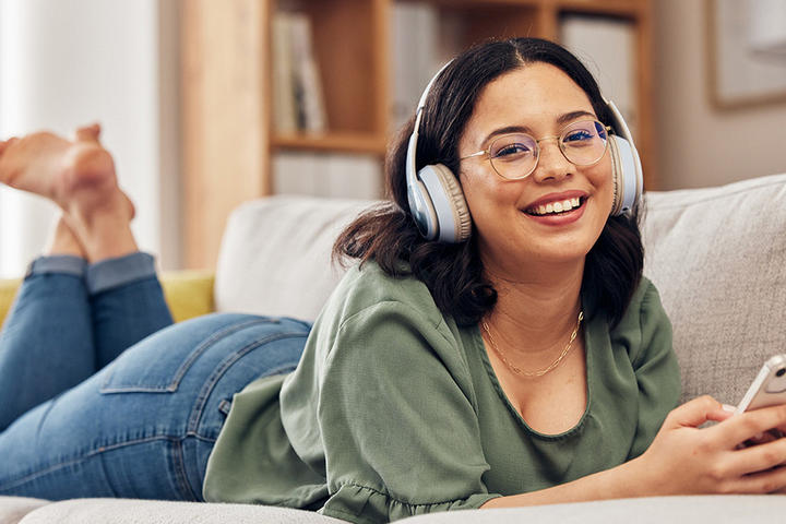 Mädchen liegt auf Bett und hört Podcast