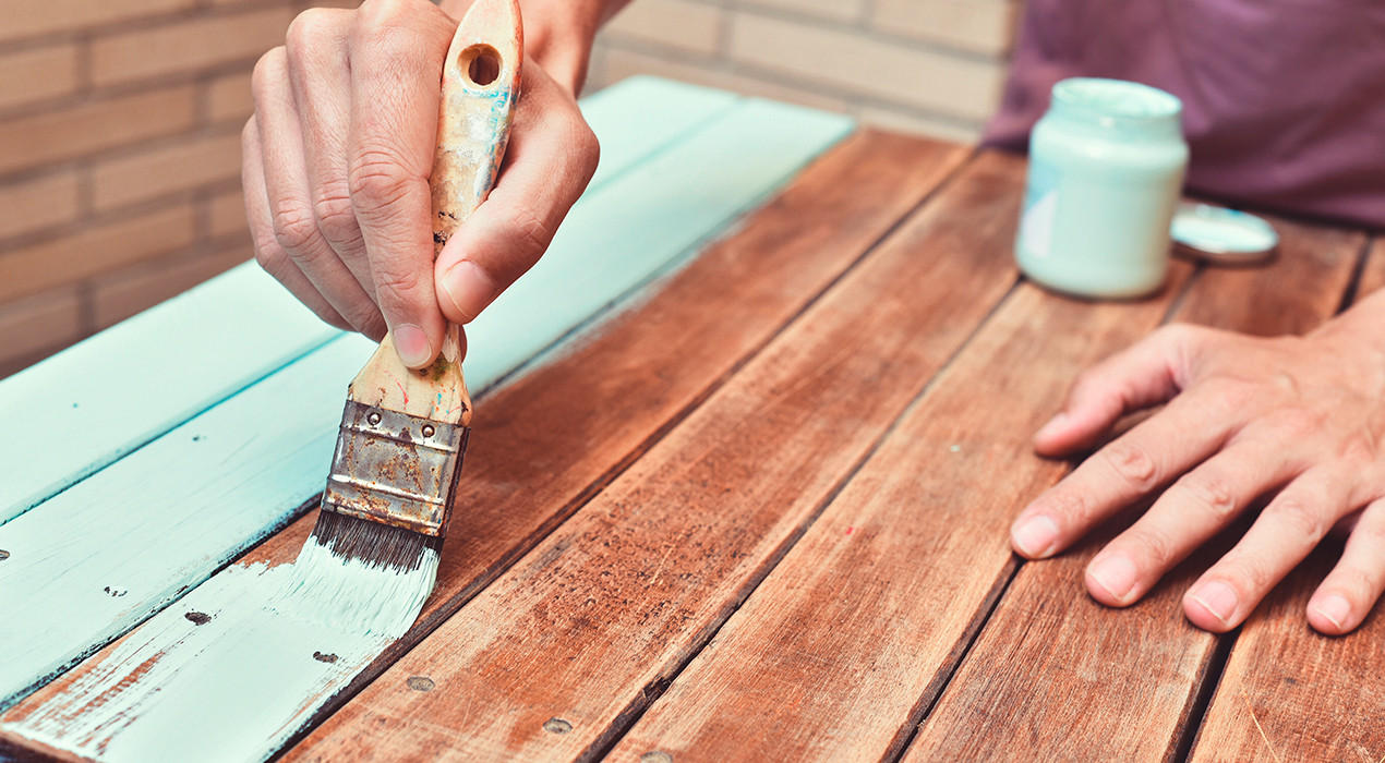 Mann streicht Holztisch türkies
