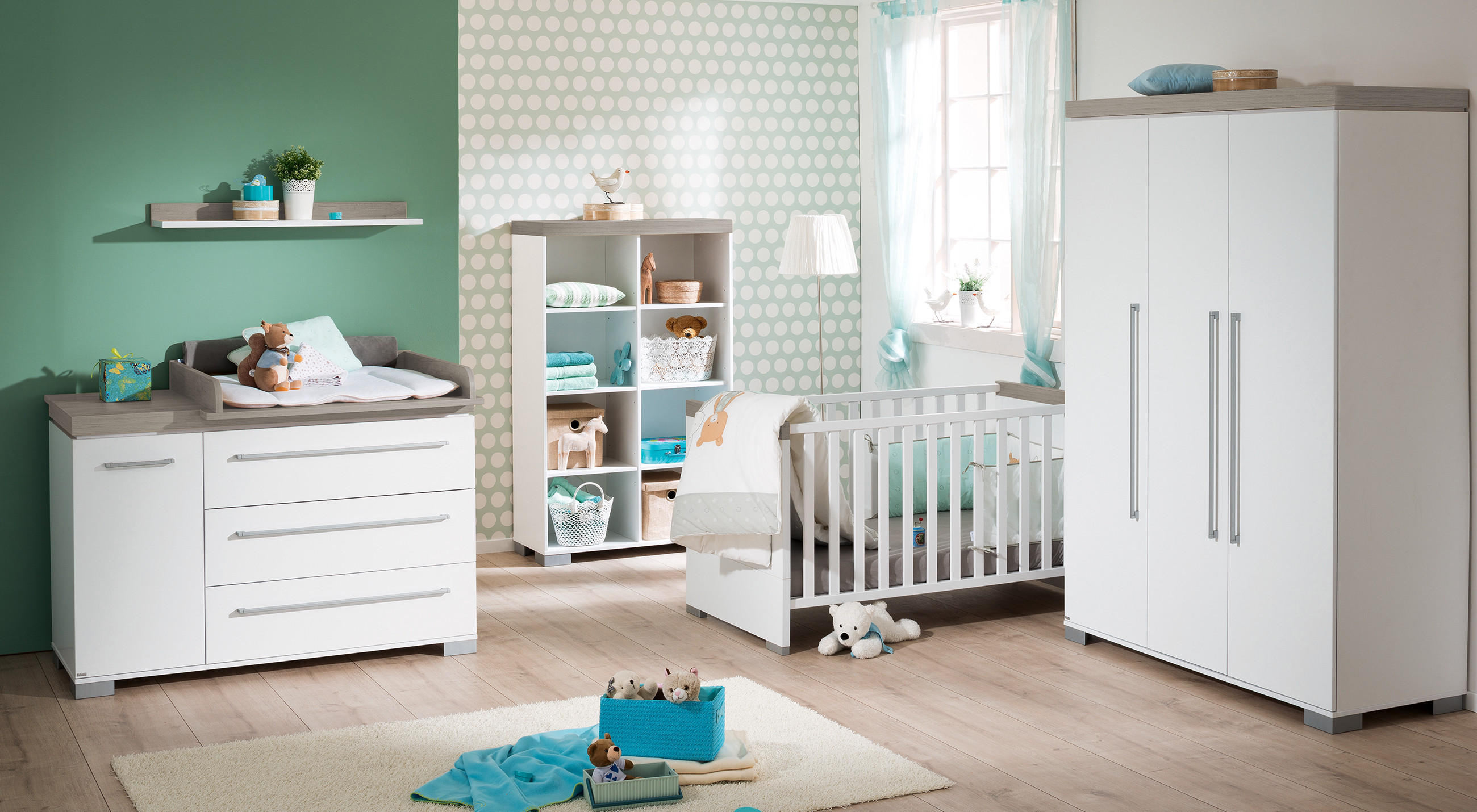 Kinderzimmer mit Wickelkommode, Regal, Kinderbett und Kleiderschrank in hellem Holz und Weiß vor grüner Wand.