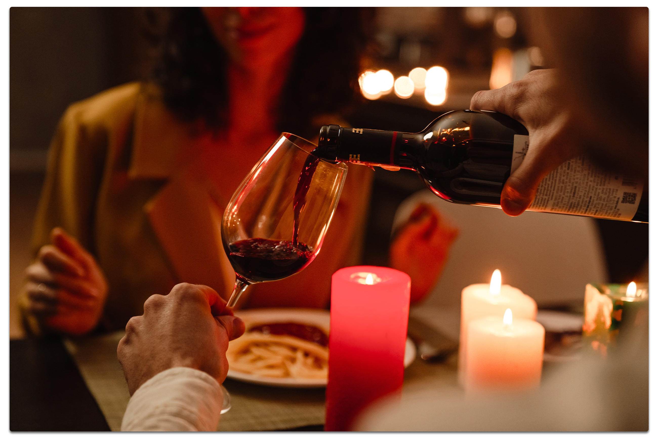 Ein Mann gießt Wein in ein Glas an einem Esstisch, während eine Frau ihm gegenüber sitzt.