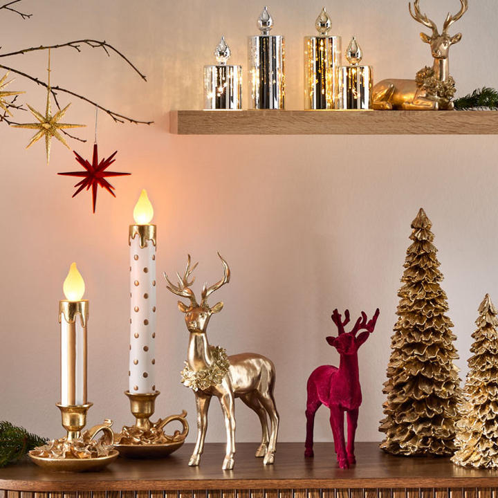 Festliche Szene mit Kerzen, goldenen und roten Rentierfiguren sowie goldenen Weihnachtsbaum-Ornamenten auf einem Holztisch.