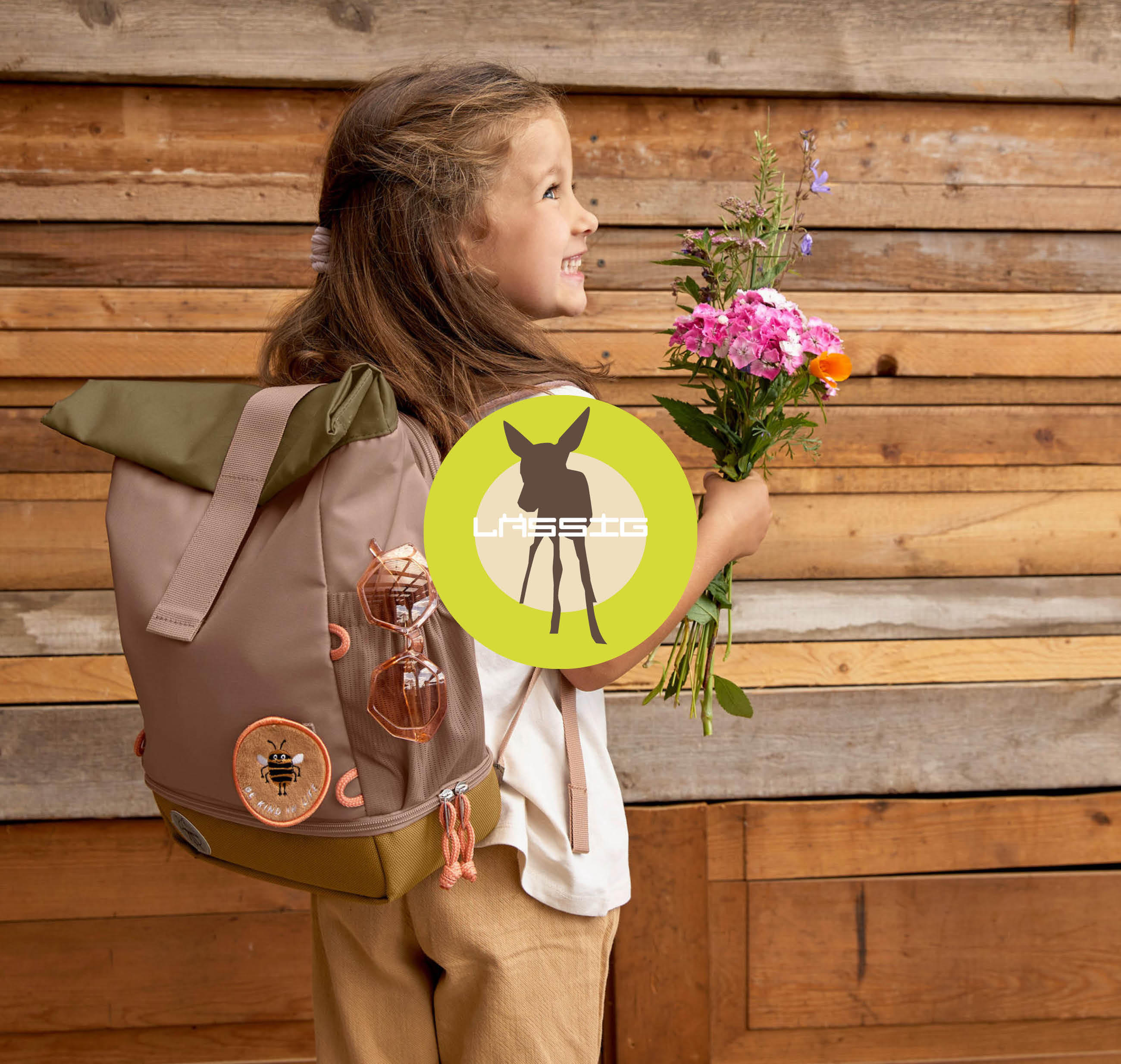 Ein Mädchen mit einem Lässig-Rucksack hält eine Blume und lächelt fröhlich.