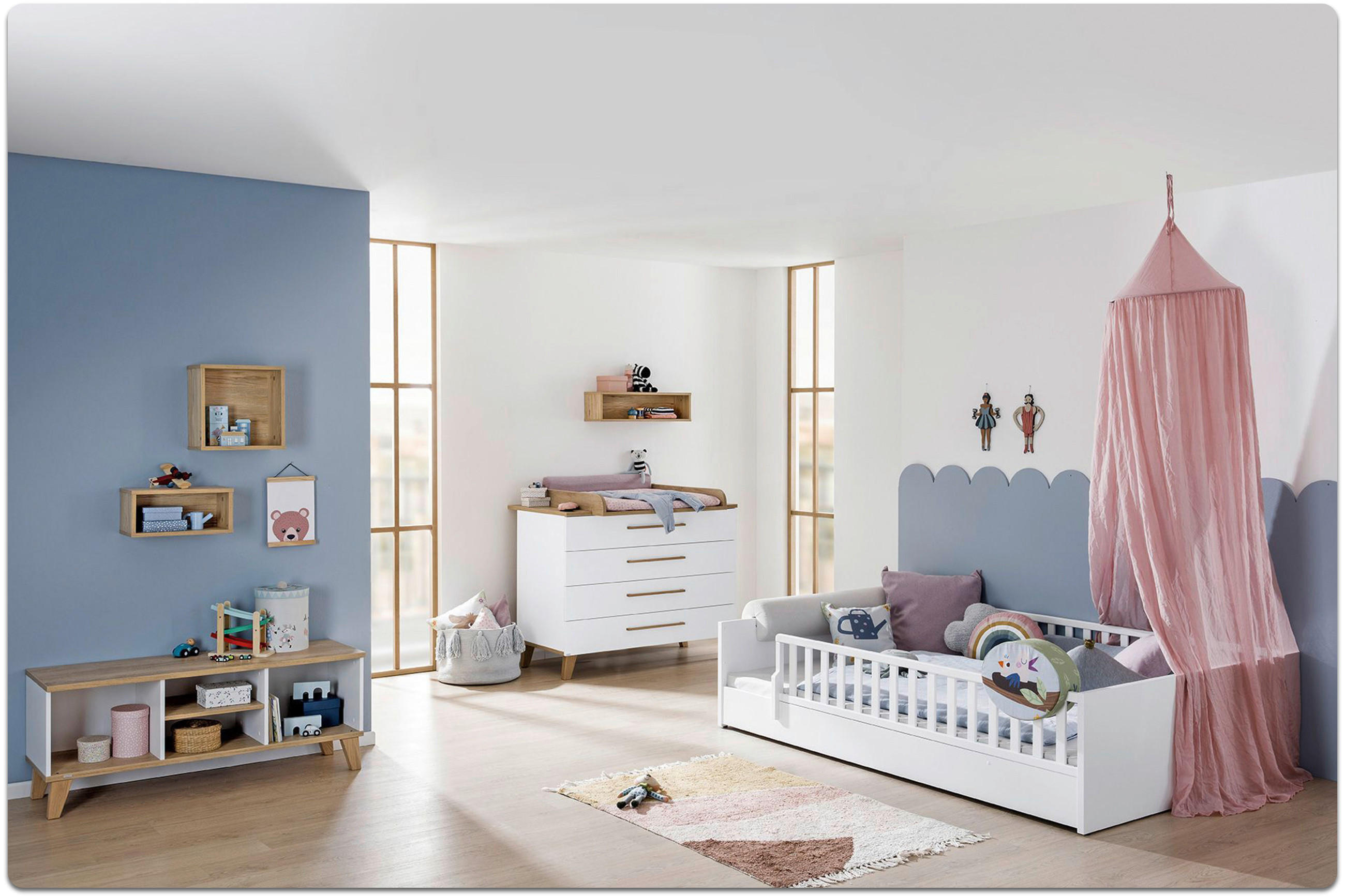 Kinderzimmer mit weißem Babybett, rosa Baldachin, Kommode, Wandregalen und blauer Wandgestaltung mit Wolkenform.