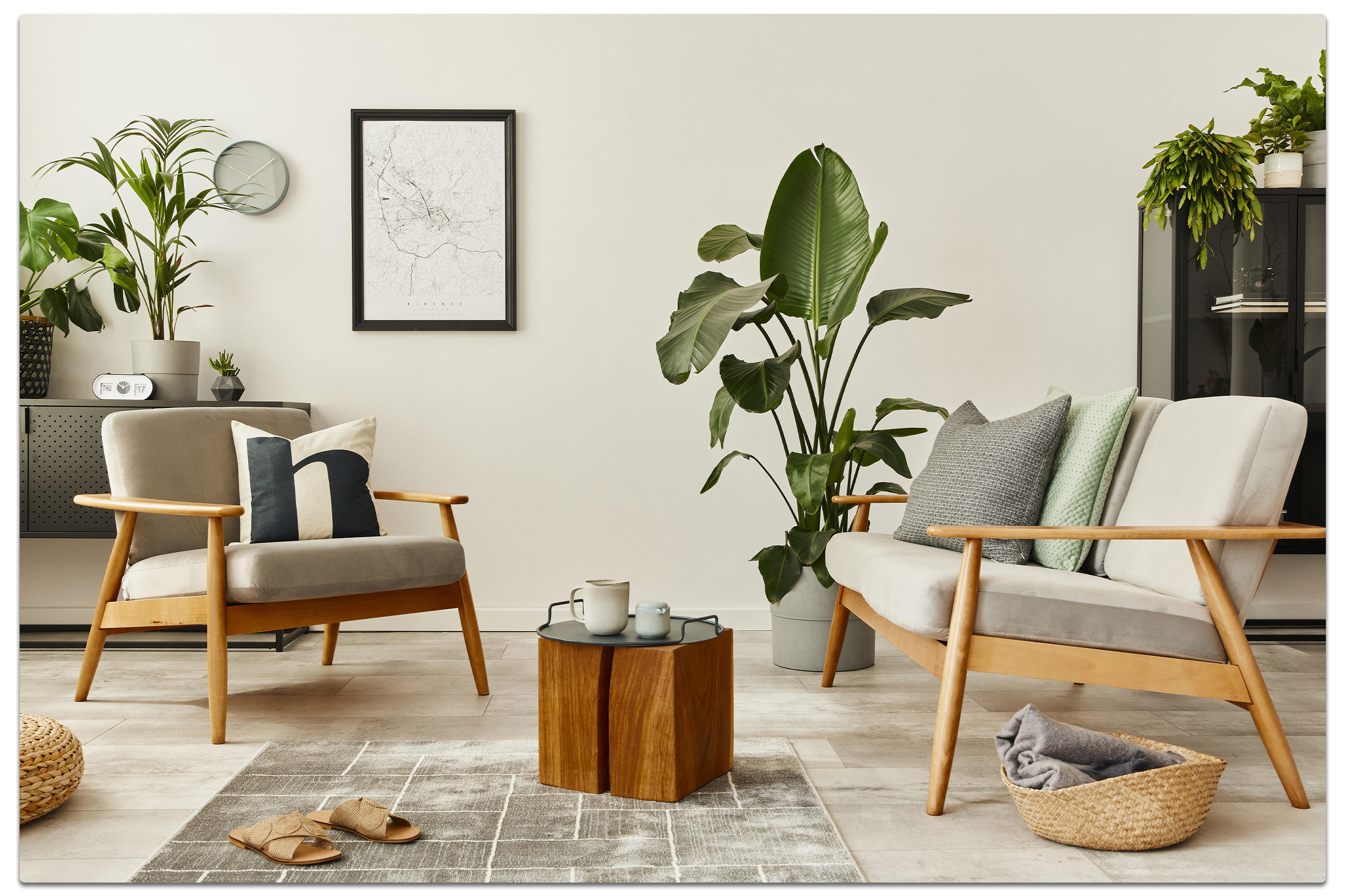 Modern eingerichtetes Wohnzimmer mit zwei Holzsesseln und grauen Polstern, kleinem Holztisch mit Teeservice sowie dekorativen Pflanzen und Wandkarte – gemütliches Ambiente für stilvolles Wohnen.