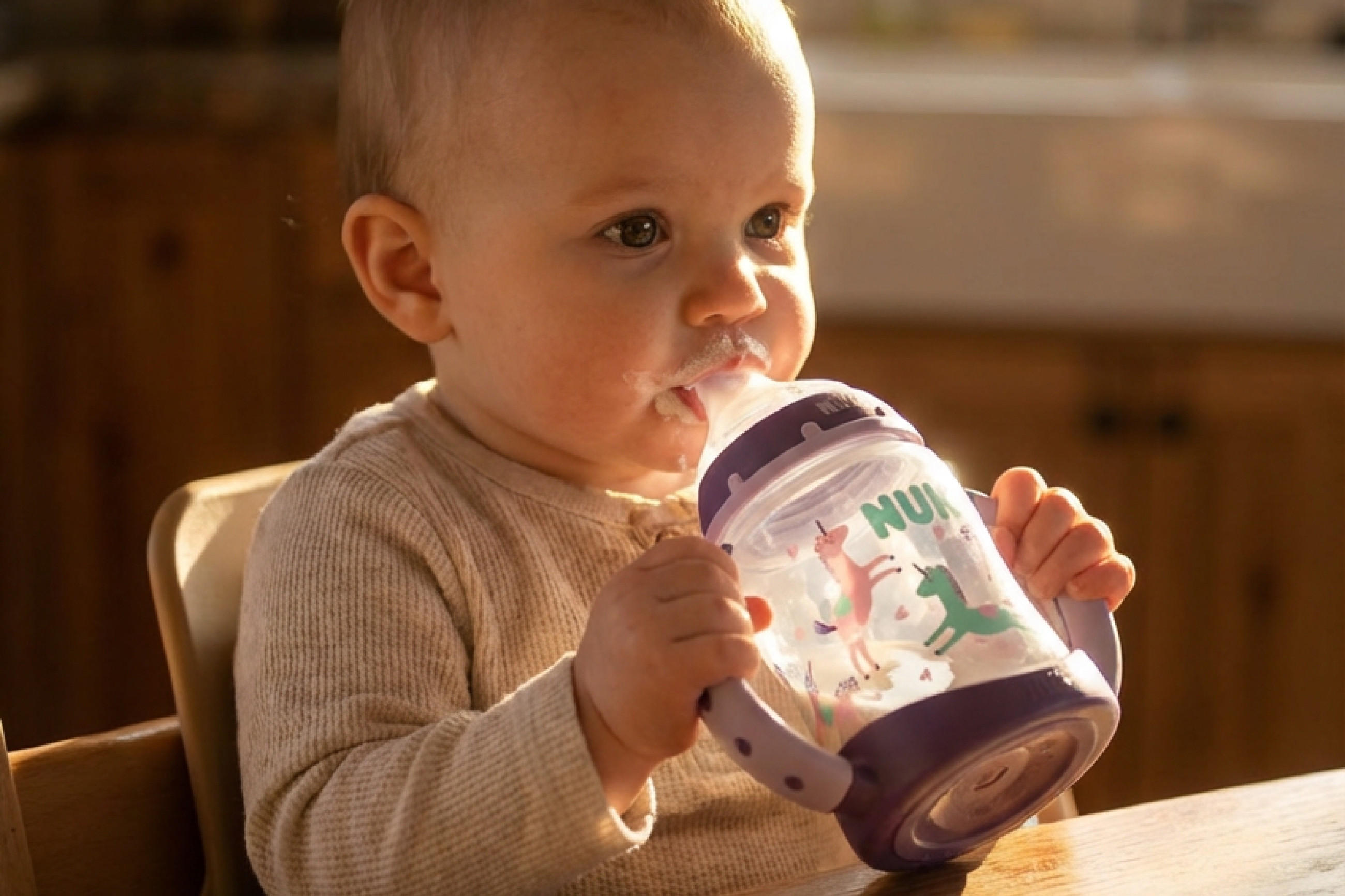 Kleinkind sitzt am Tisch und hält eine Trinkflasche mit bunten Tiermotiven.