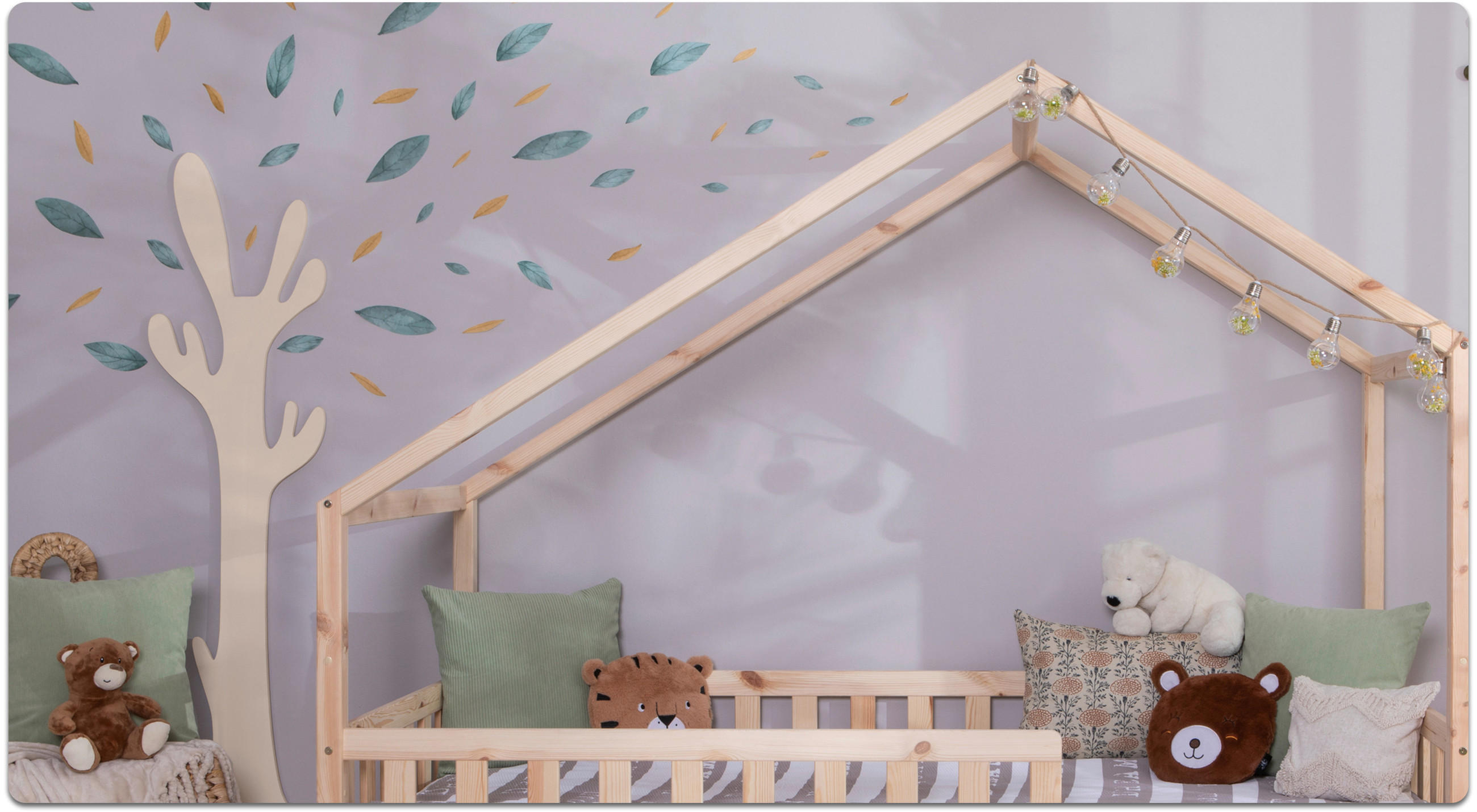Kinderzimmer mit einem hölzernen Bett in Hausform, mehreren Kissen, Plüschtieren und einer Wanddekoration in Form eines Baumes mit Blättern