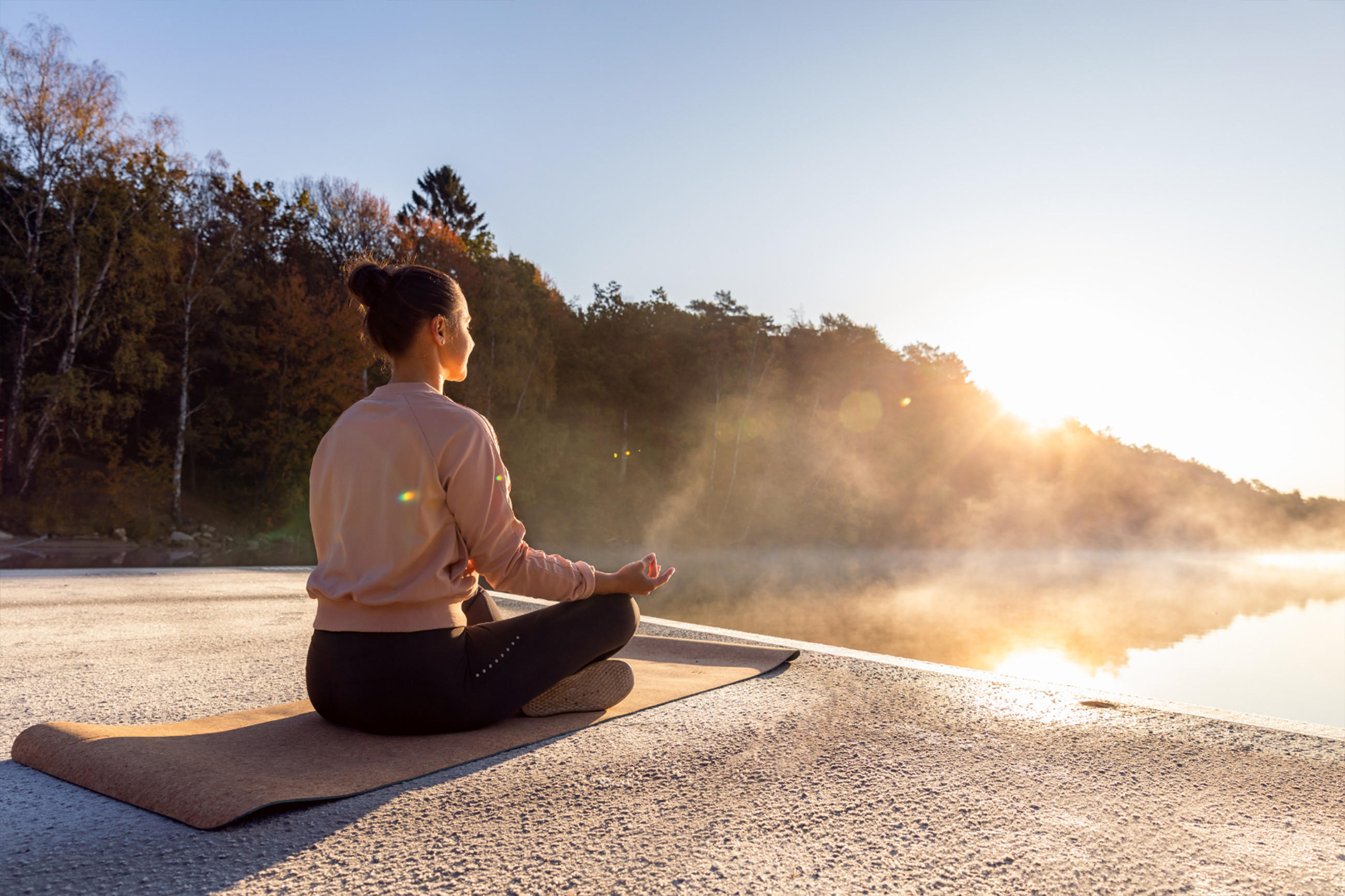 Meditierende Frau in Yoga-Haltung am See, umgeben von der beruhigenden Natur und Wasser