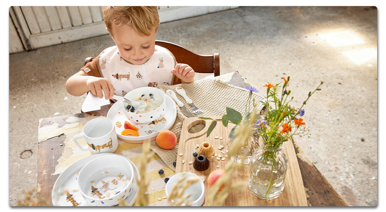 Kind mit Lätzchen und Kinderbesteck am Esstisch