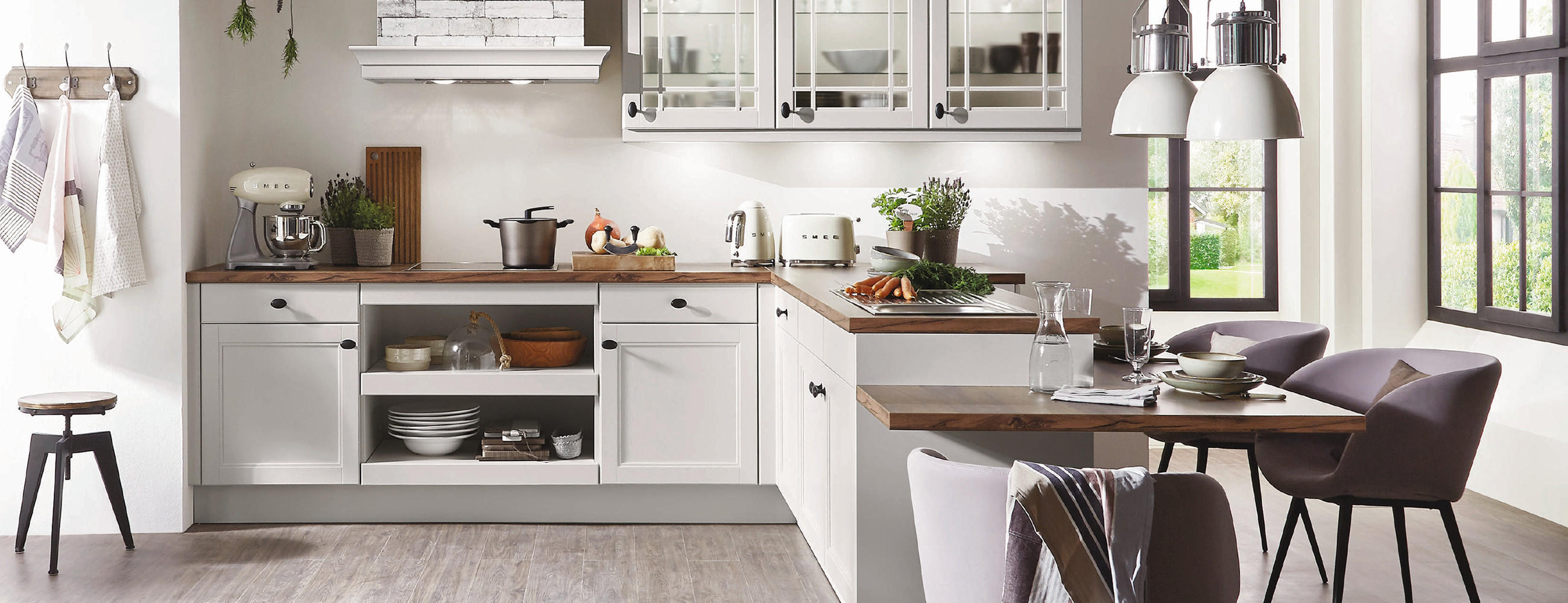 Klassische Küche in L-Form mit hellen Fronten und dunkler Arbeitsplatte und Sitzgruppe als Anbau.