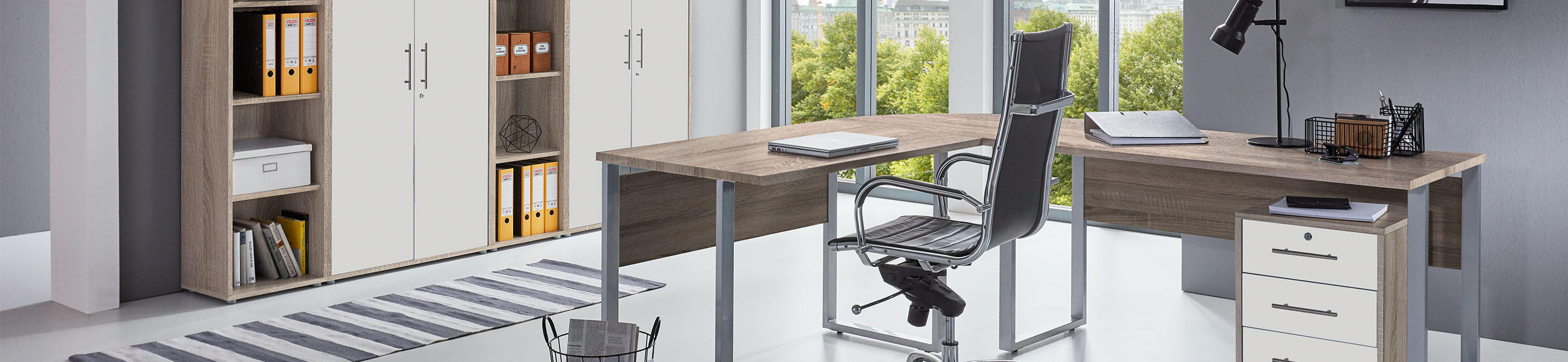 Modernes Büro mit Eckschreibtisch, Bürostuhl, Rollcontainer und Aktenschränken aus Eiche und weiß matt vor großen Fenstern