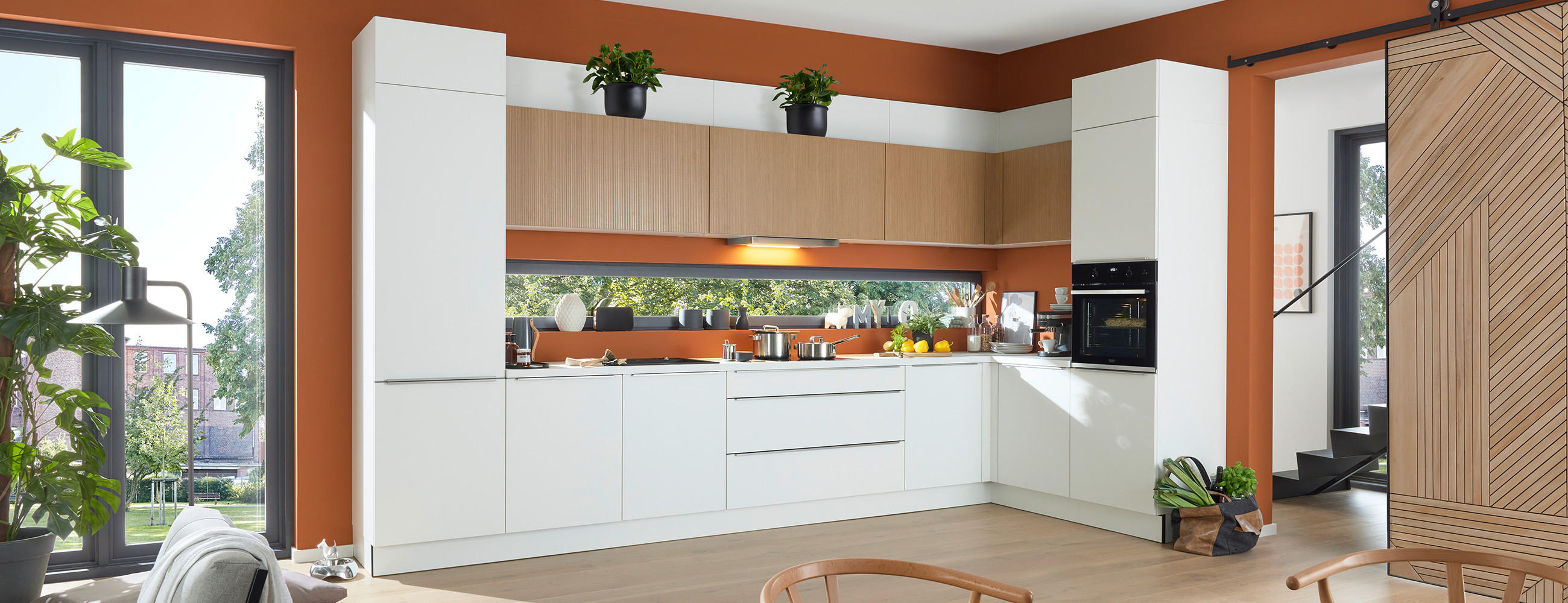 Weiße Küche in L-Form mit grifflosen Fronten und Holzelementen.