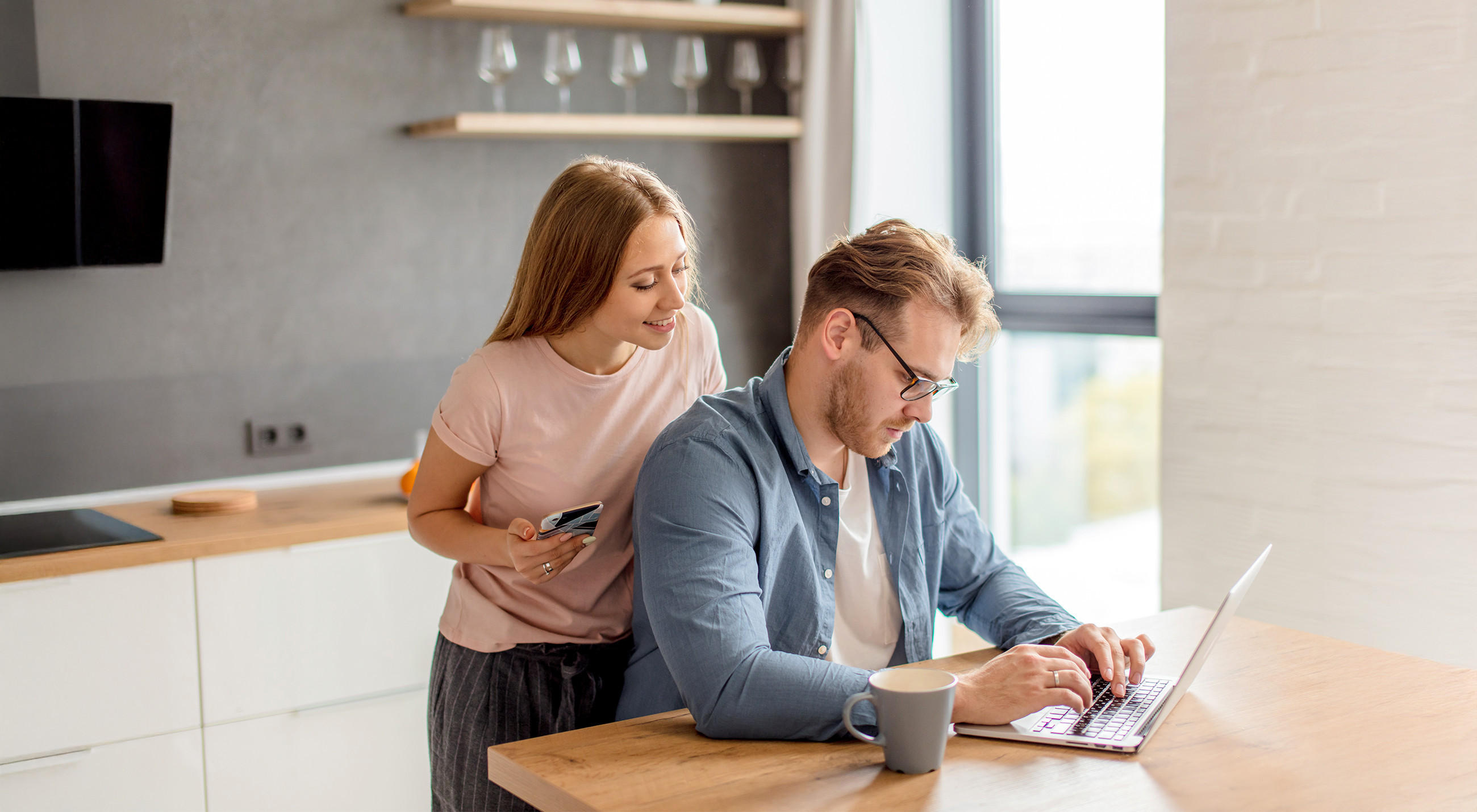 Ein Mann und eine Frau sitzen an einem Tisch mit einem Laptop und planen Küche online.