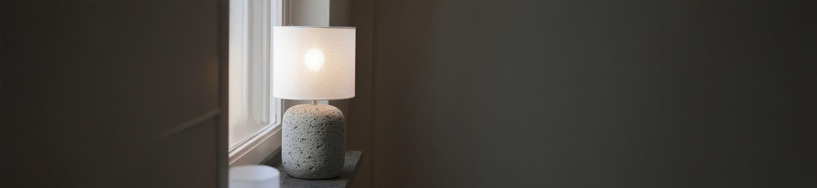 Betonlampe mit weißem Lampenschirm auf einer Fensterbank