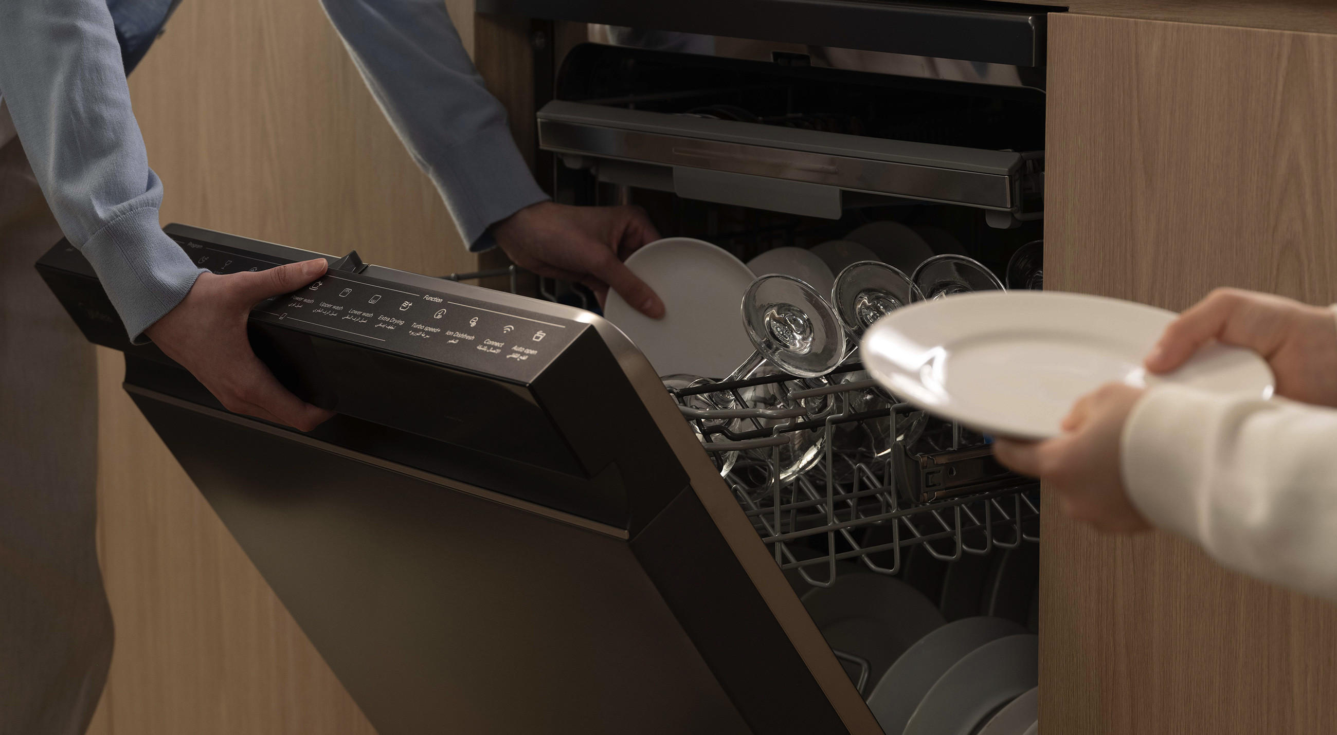 Nahaufnahme eines geöffneten Midea-Geschirrspülers: Hände räumen Teller und Gläser in die Körbe ein, das Bedienfeld in der Tür ist sichtbar.