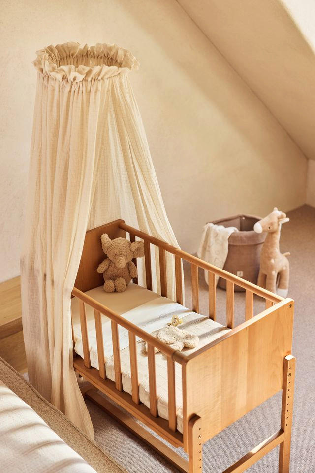 Otroška posteljica s baldahinom in medvedkom, pripravljena za spanje.