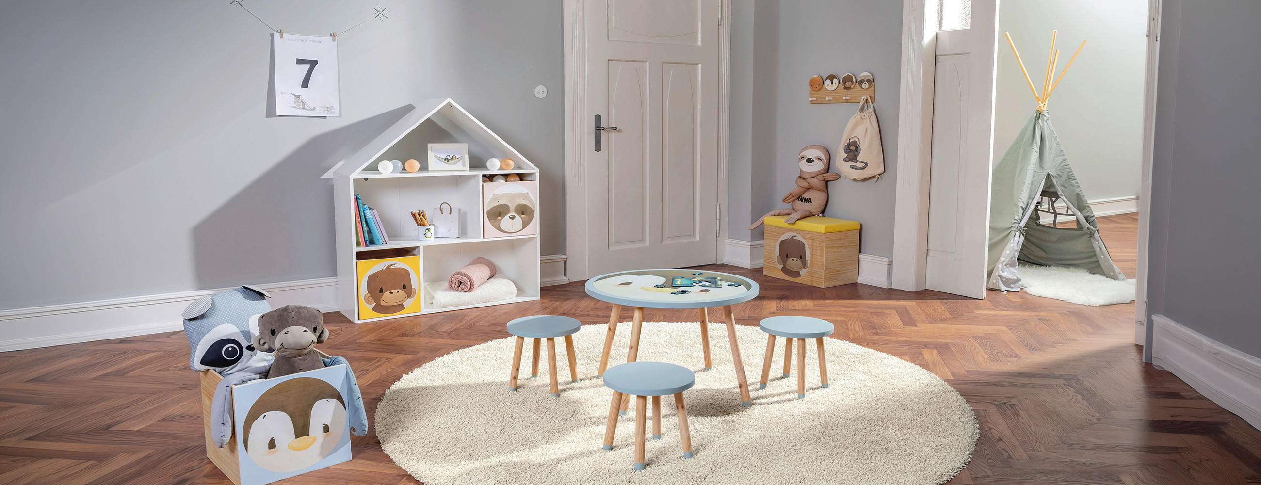 Kinderspielzimmer mit rundem Teppich, kleinem Tisch mit vier Hockern, Spielzeugregal in Hausform und Kuscheltieren.