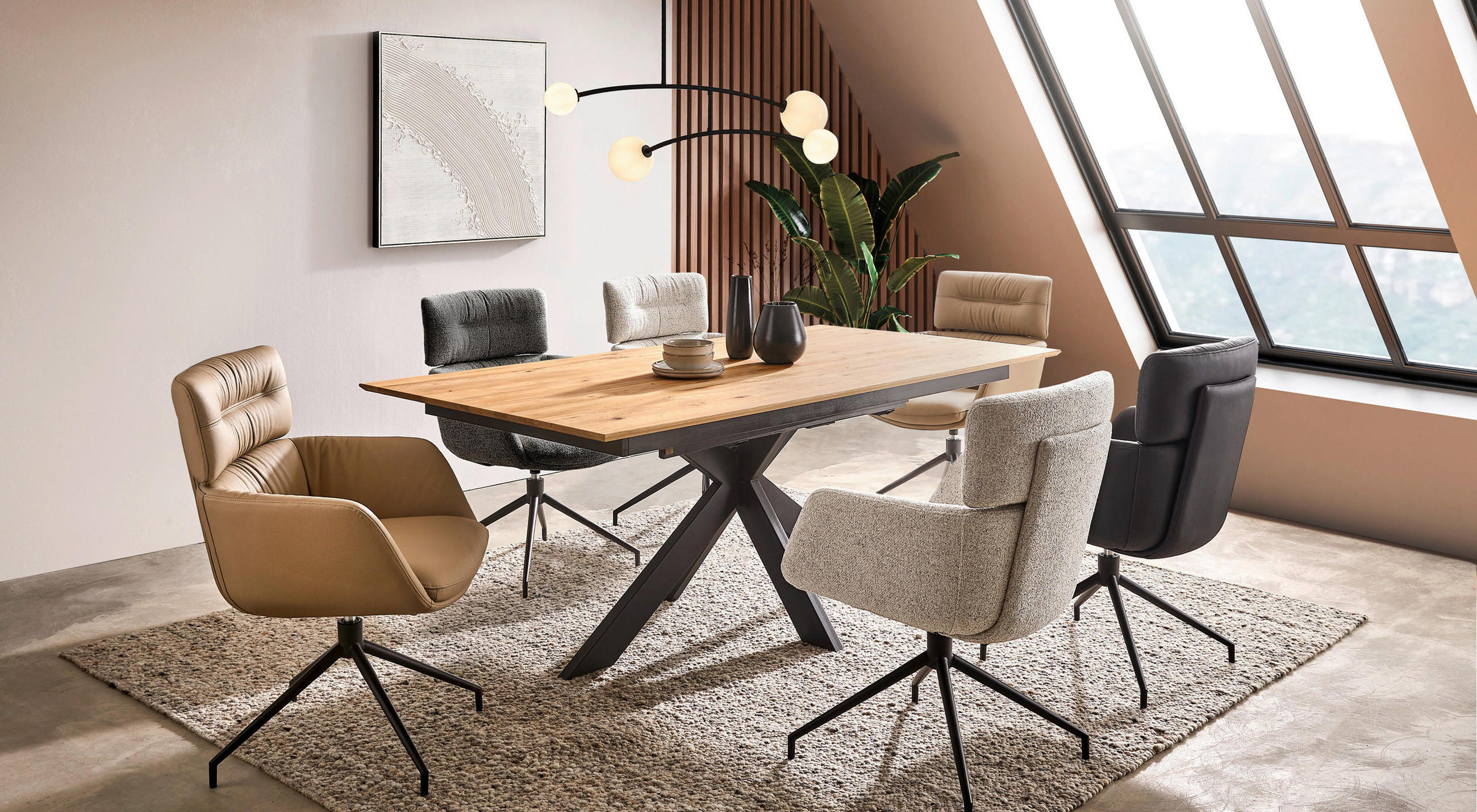 Esstisch aus Eiche mit schwarzem Tischbein in Dachgeschosswohnung mit großer Fensterfront. Stühle in beige, braun und schwarz stehen um den Esstisch.