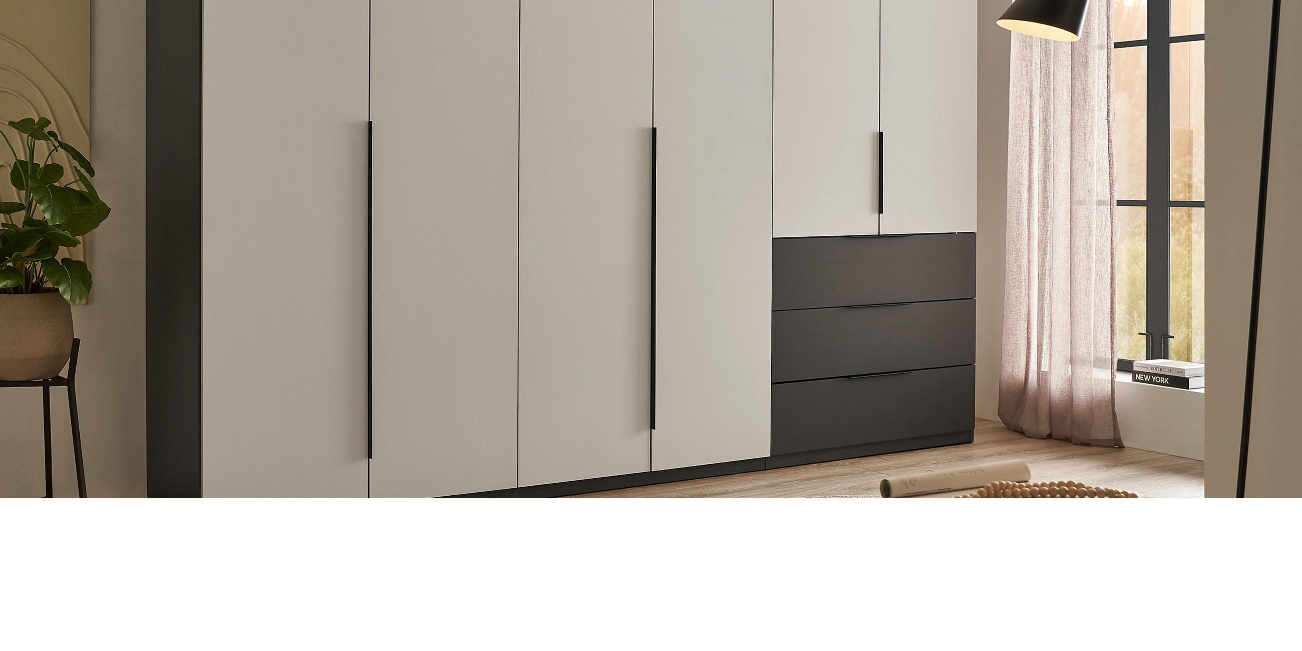 Kleiderschrank in beige mit dunkelgrauen Seitenwänden und Schubladen mit schwarzer Lampe im Vordergrund.